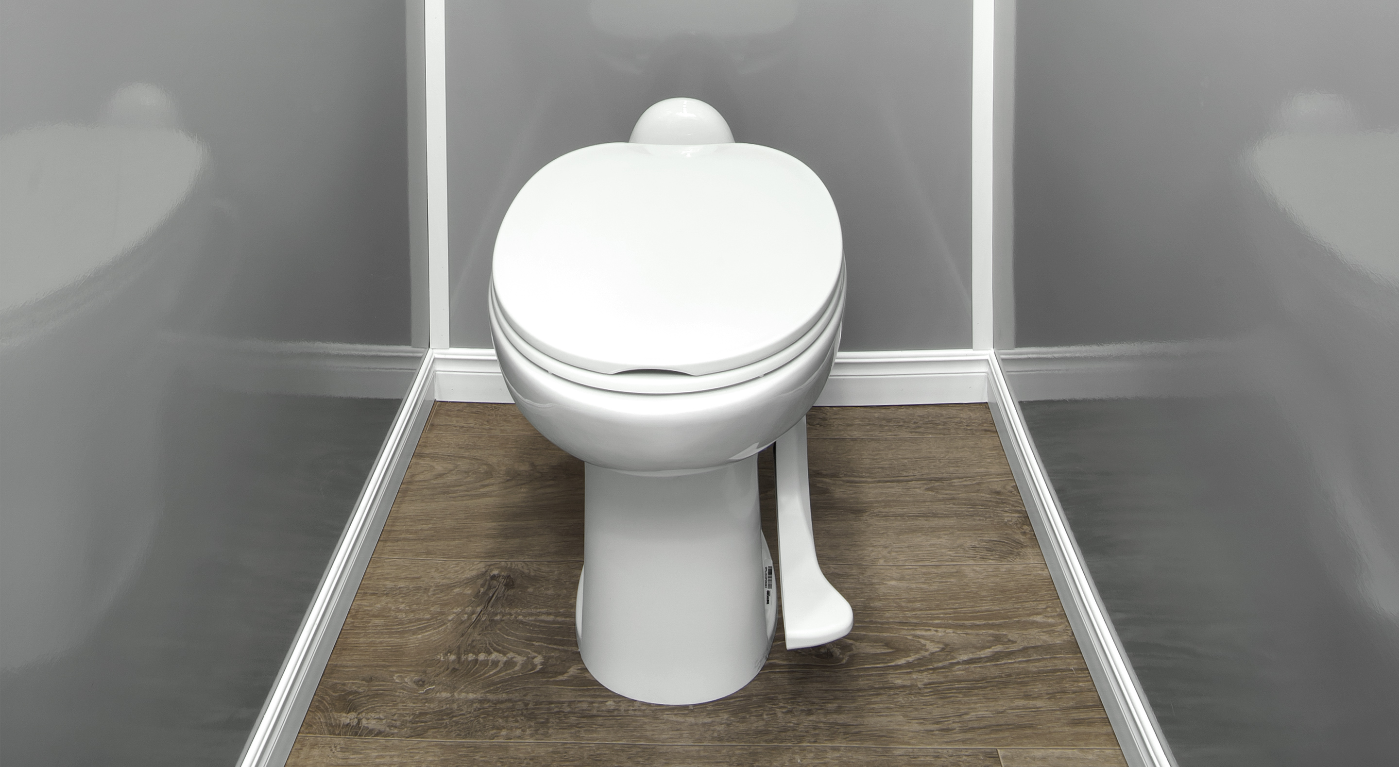 White toilet with closed lid and foot pedal flush on a wood floor and gray walls.
