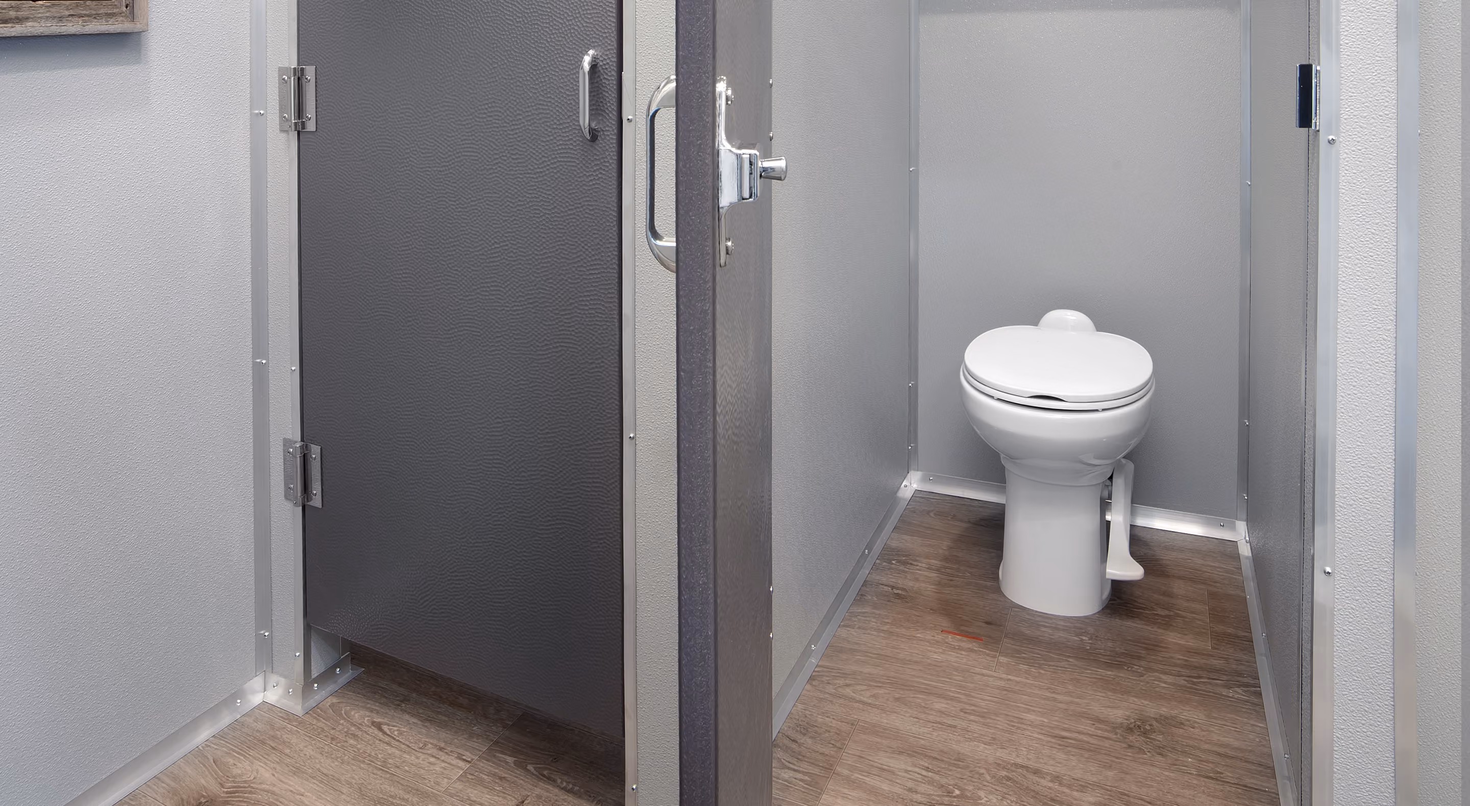 Modern commercial restroom stall with a white toilet and gray partition walls on wood flooring.
