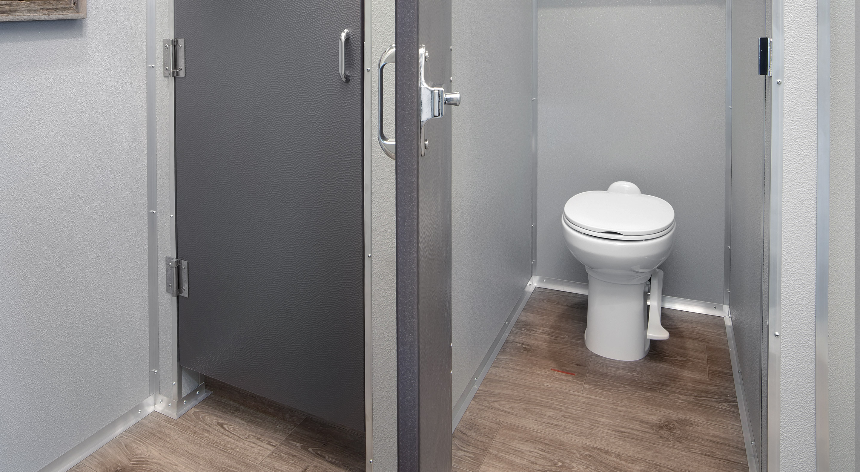 Modern commercial restroom stall with a white toilet and gray partition walls on wood flooring.
