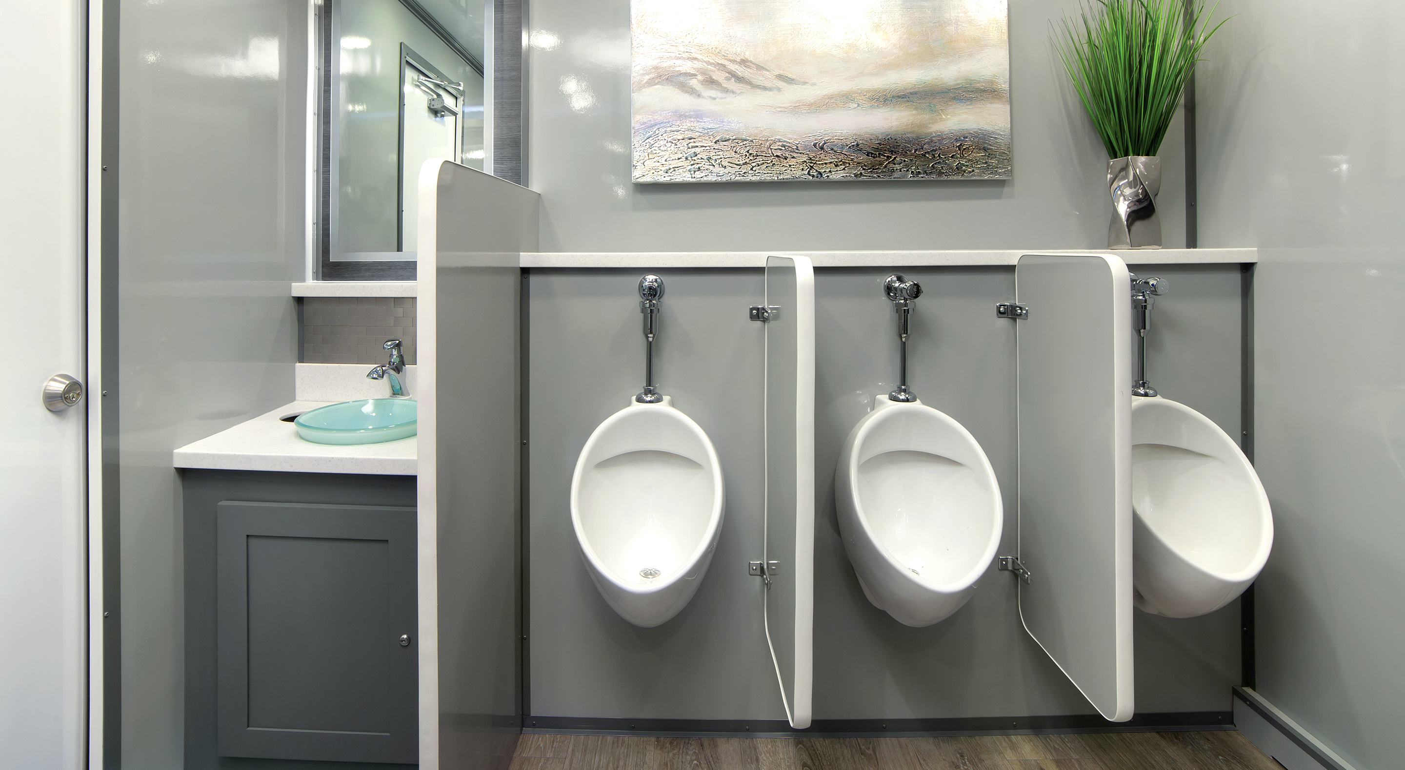 Modern restroom with three white urinals, a sink, and decorative wall art.