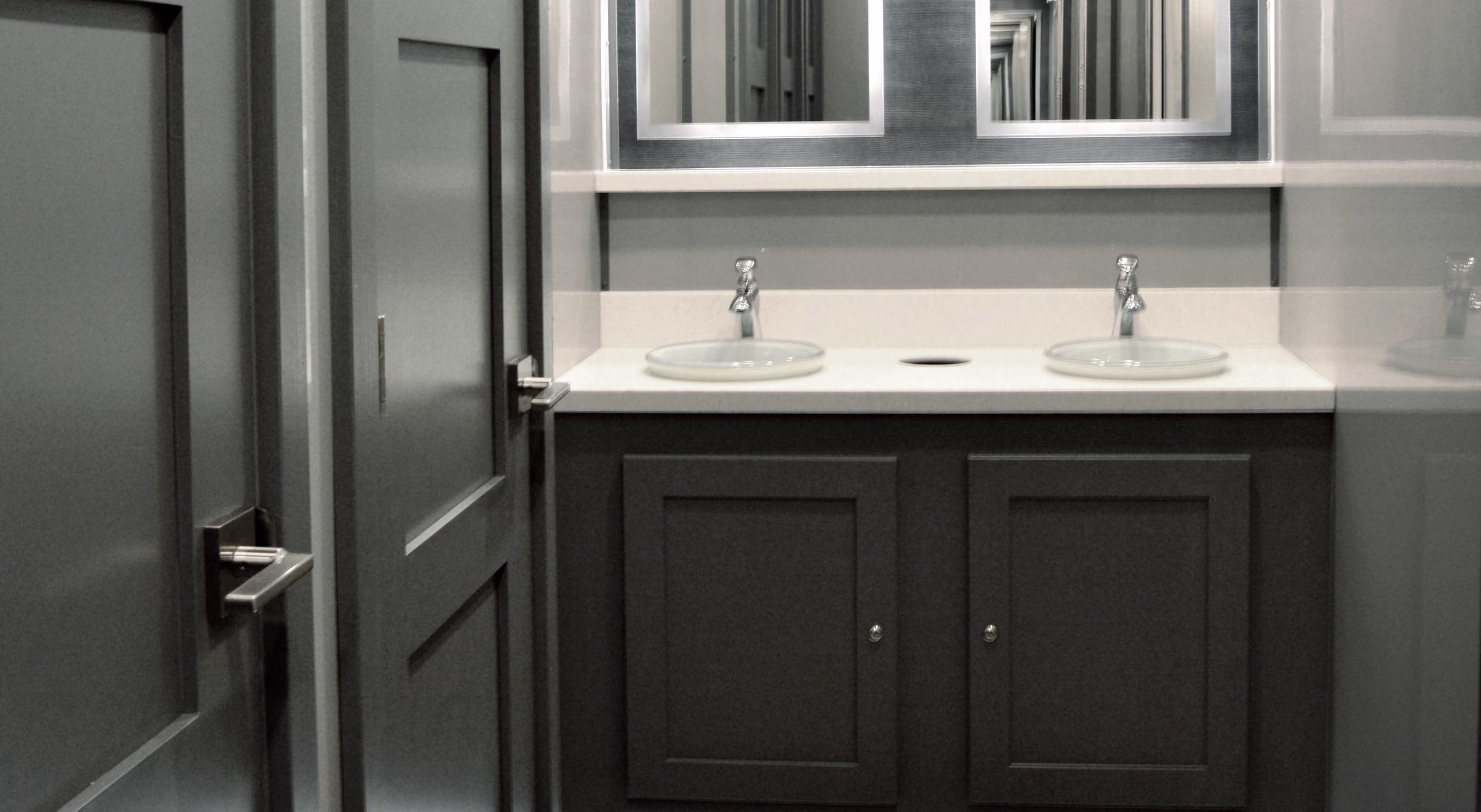 Modern bathroom vanity with two glass sinks, silver faucets, and dark cabinetry under a large mirror.