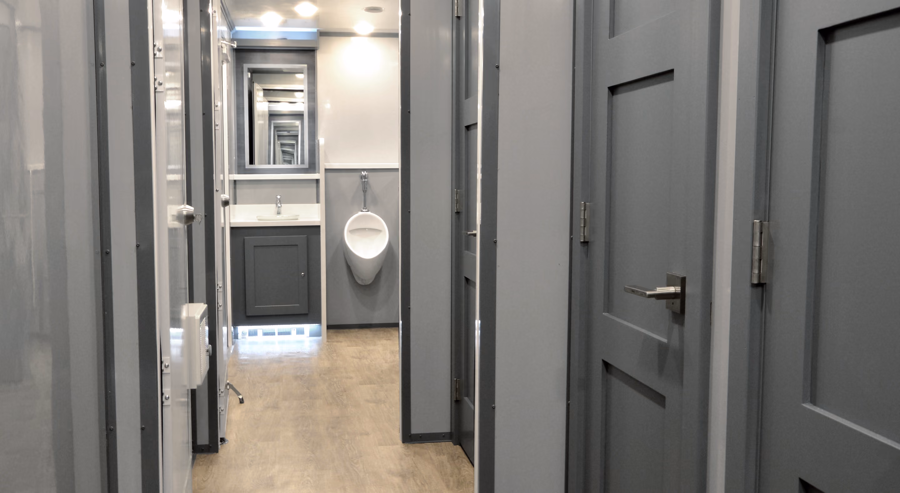Modern hallway featuring gray walls and doors, leading to a restroom with a sink and urinal.