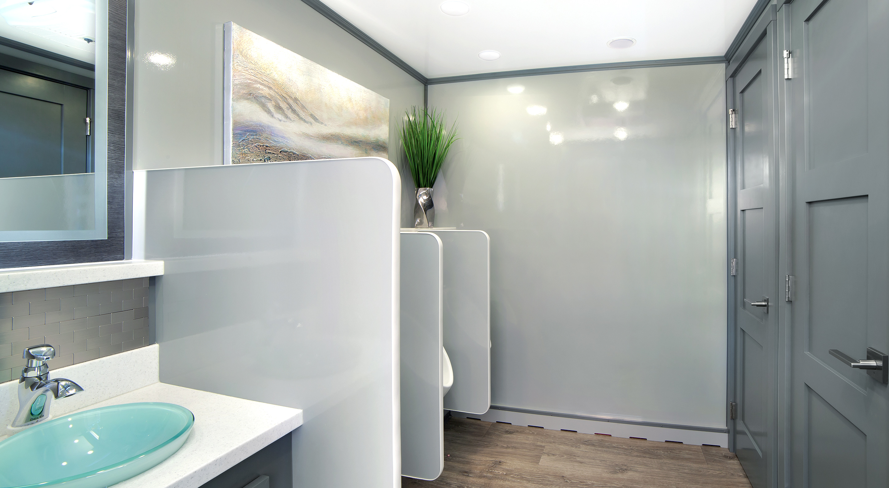 Modern restroom with green sink, white partitions, urinals, gray doors, and a potted plant.