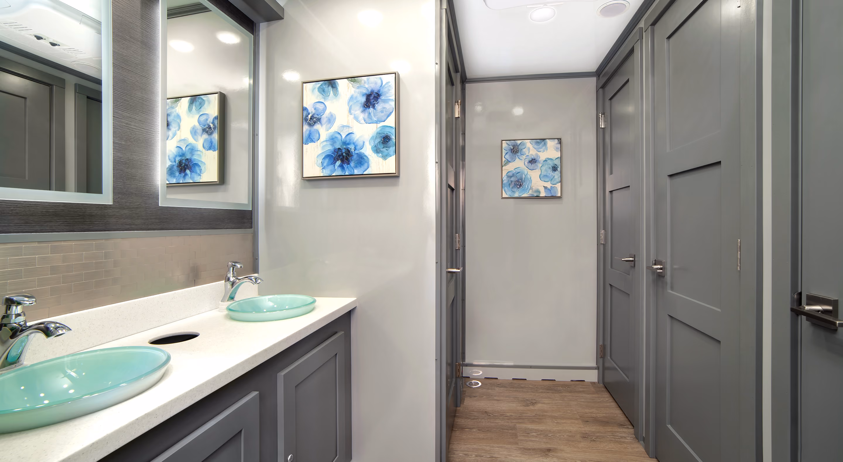 Modern bathroom with gray walls, dual sinks, and blue floral artwork on the wall.