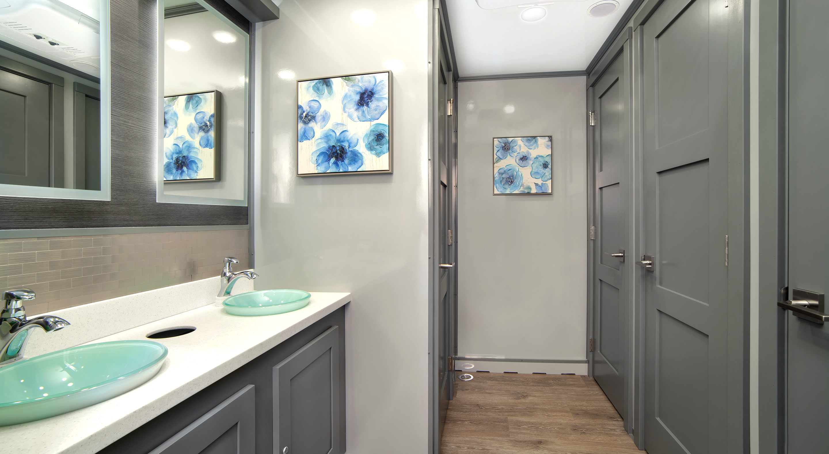 Modern bathroom with gray walls, dual sinks, and blue floral artwork on the wall.