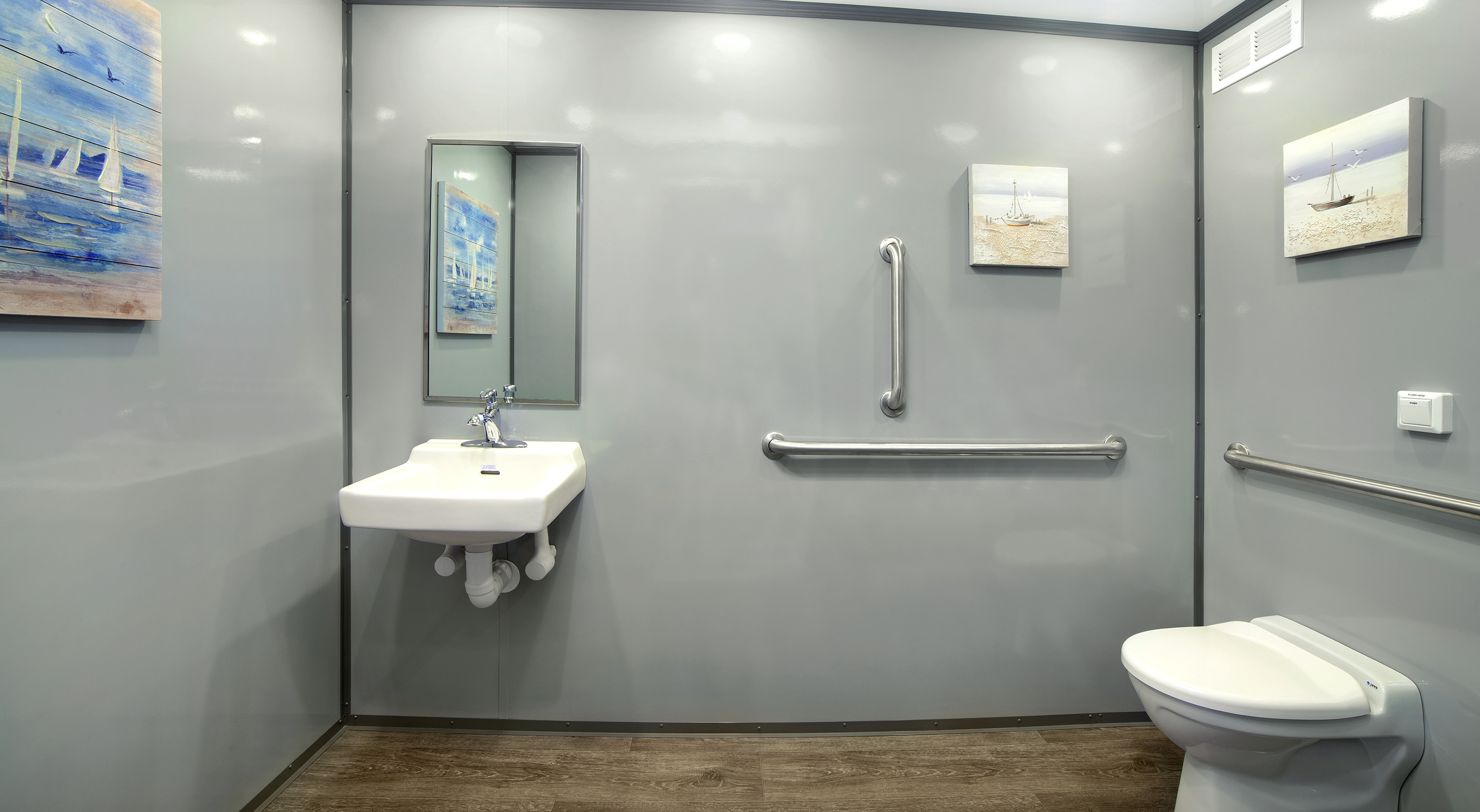 Accessible bathroom with a sink, toilet, grab bars, and art on the walls.