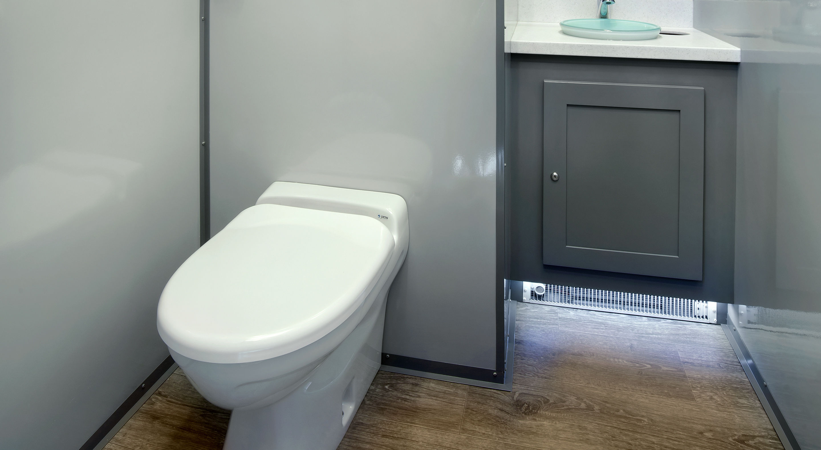 White toilet in a small bathroom with gray walls, a cabinet, and wood-patterned floor.