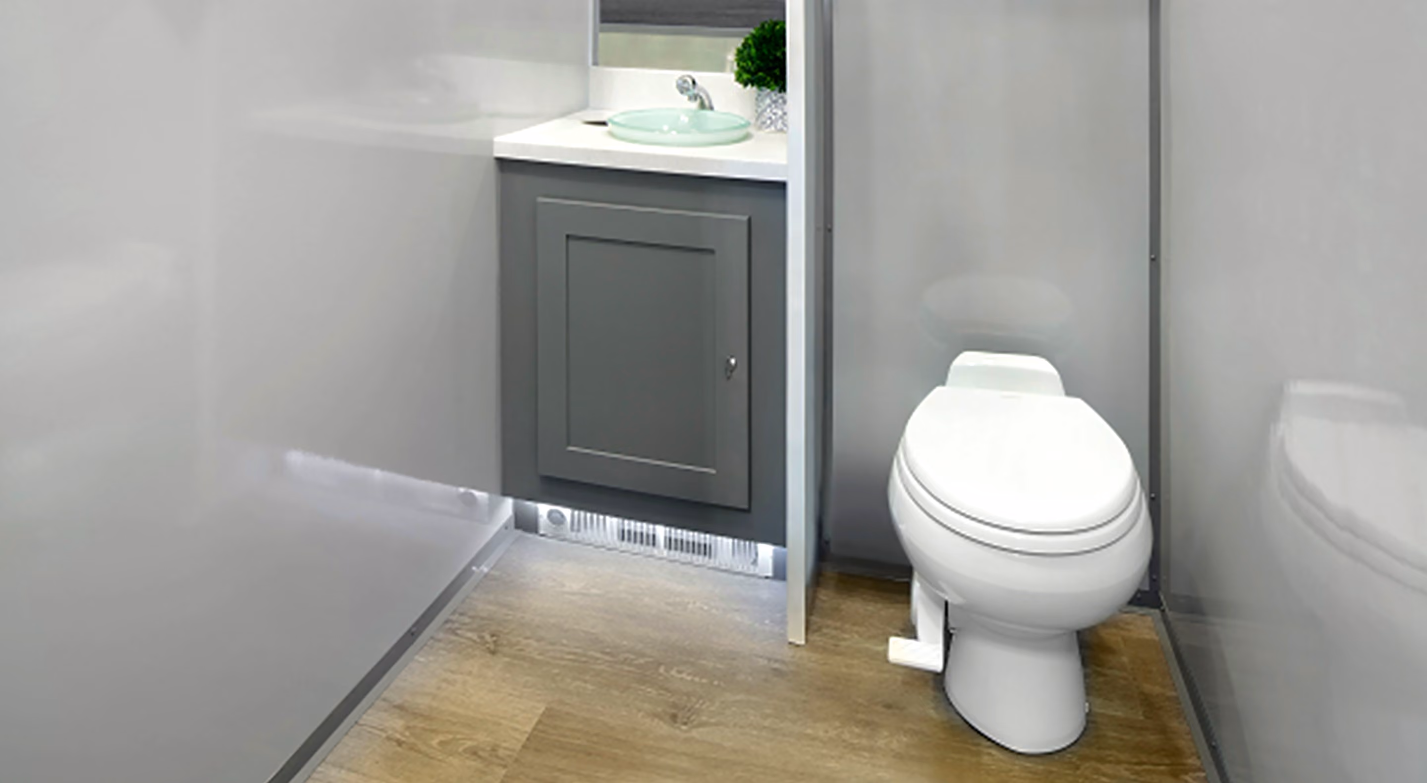 Compact bathroom with white toilet, gray cabinet, glass sink, and wood-look floor.