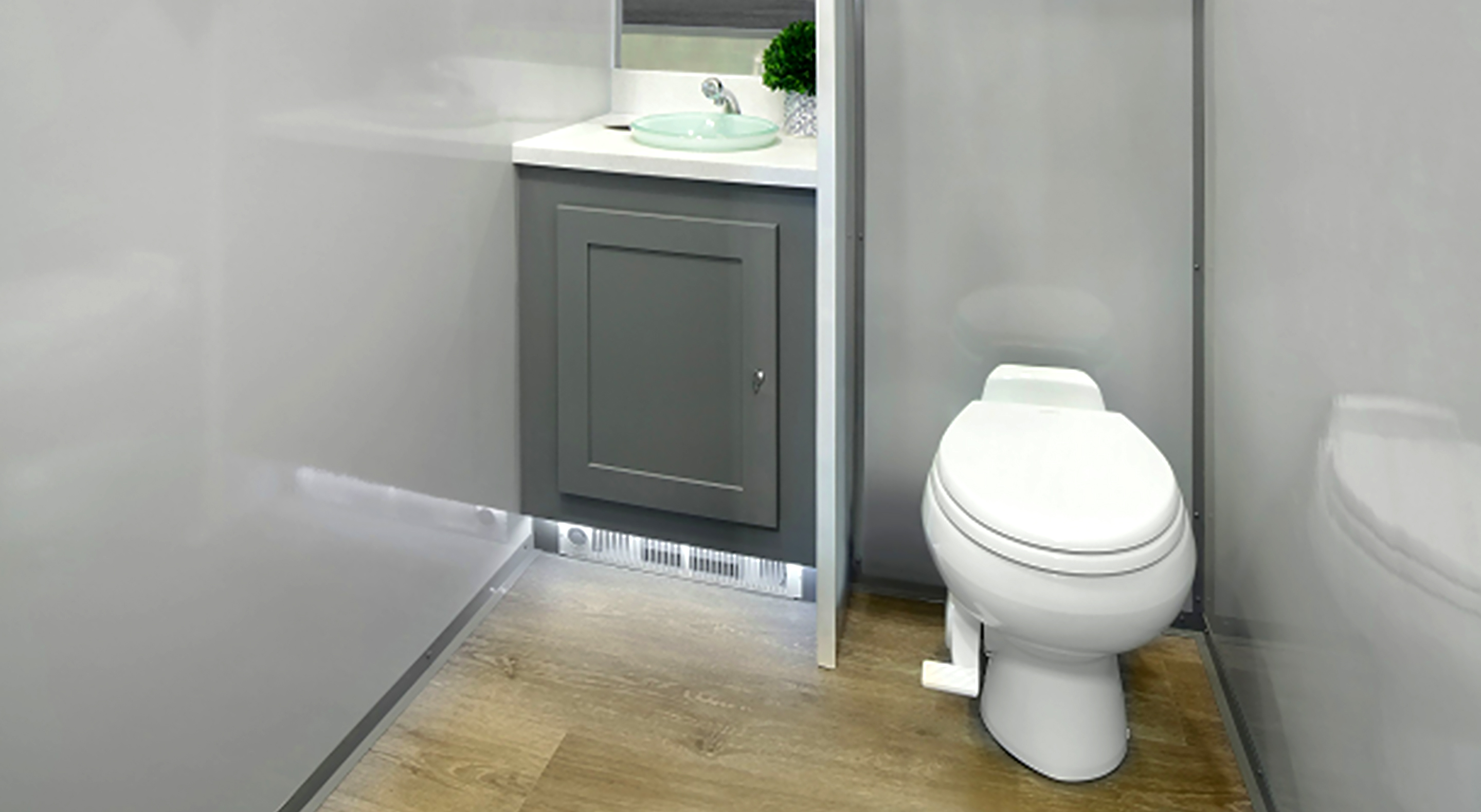 Compact bathroom with white toilet, gray cabinet, glass sink, and wood-look floor.