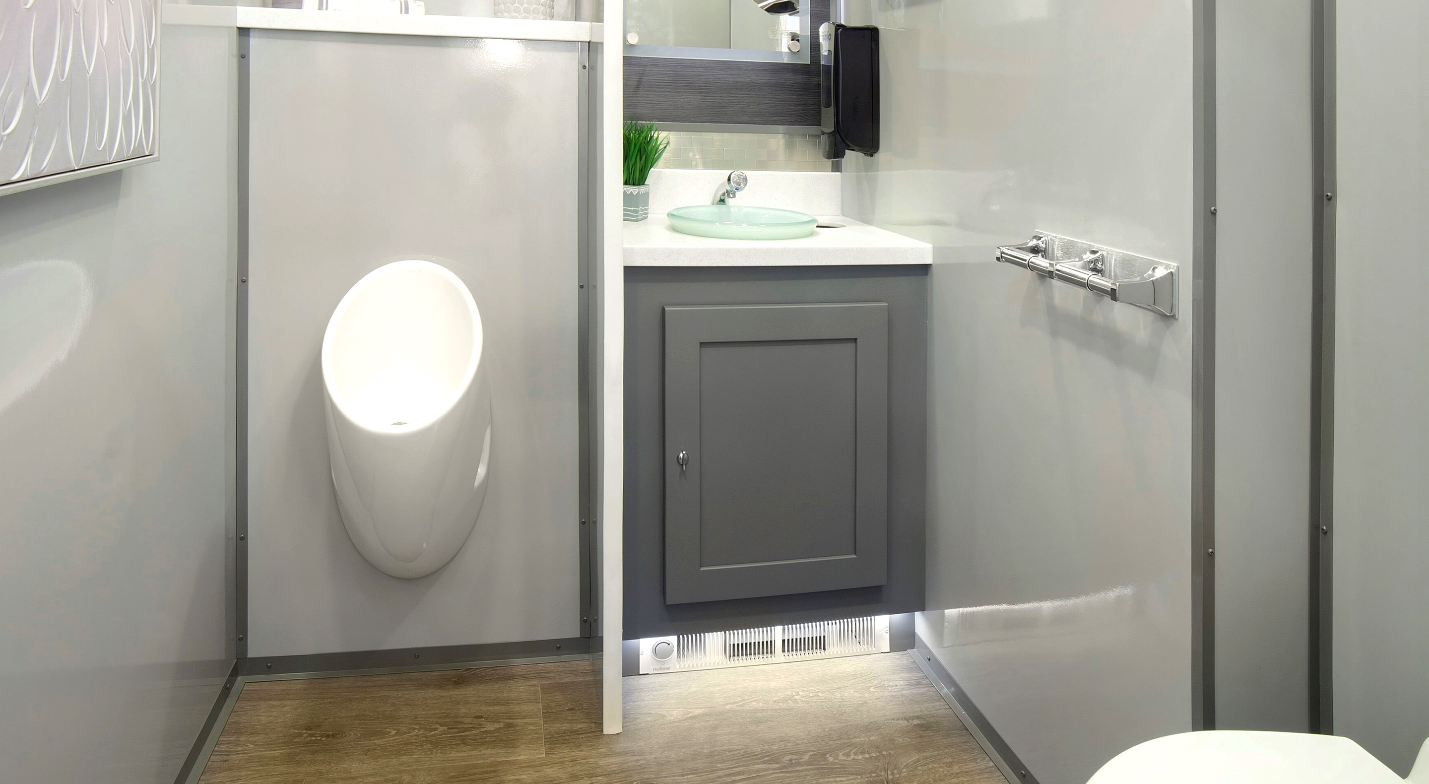Modern restroom interior featuring a wall-mounted urinal, sink, and grey cabinetry.