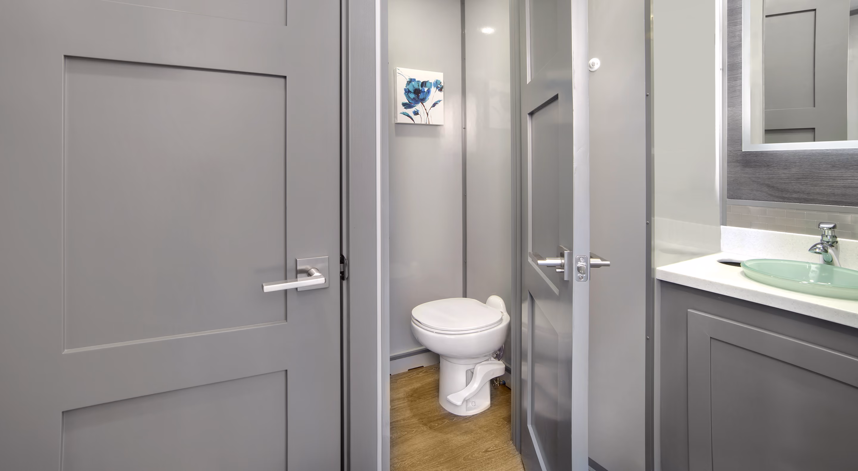 Small bathroom with a white toilet, gray walls, gray door, and a sink with a green glass basin.