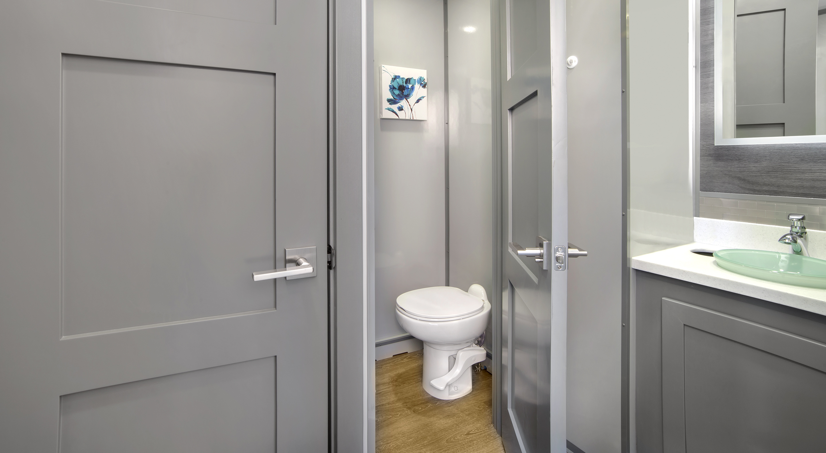 Small bathroom with a white toilet, gray walls, gray door, and a sink with a green glass basin.