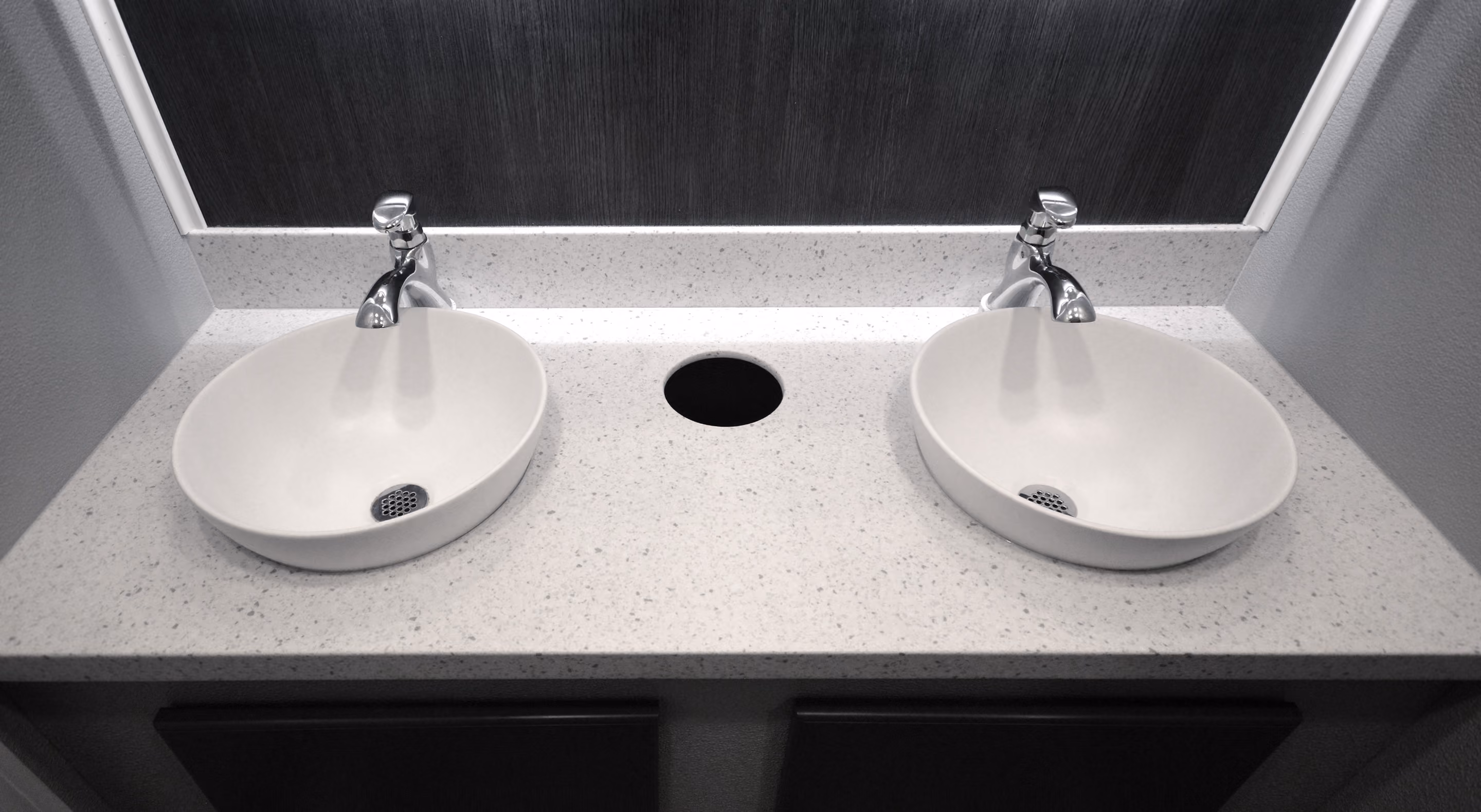Double white oval sinks with chrome faucets on a speckled white countertop and dark backsplash.