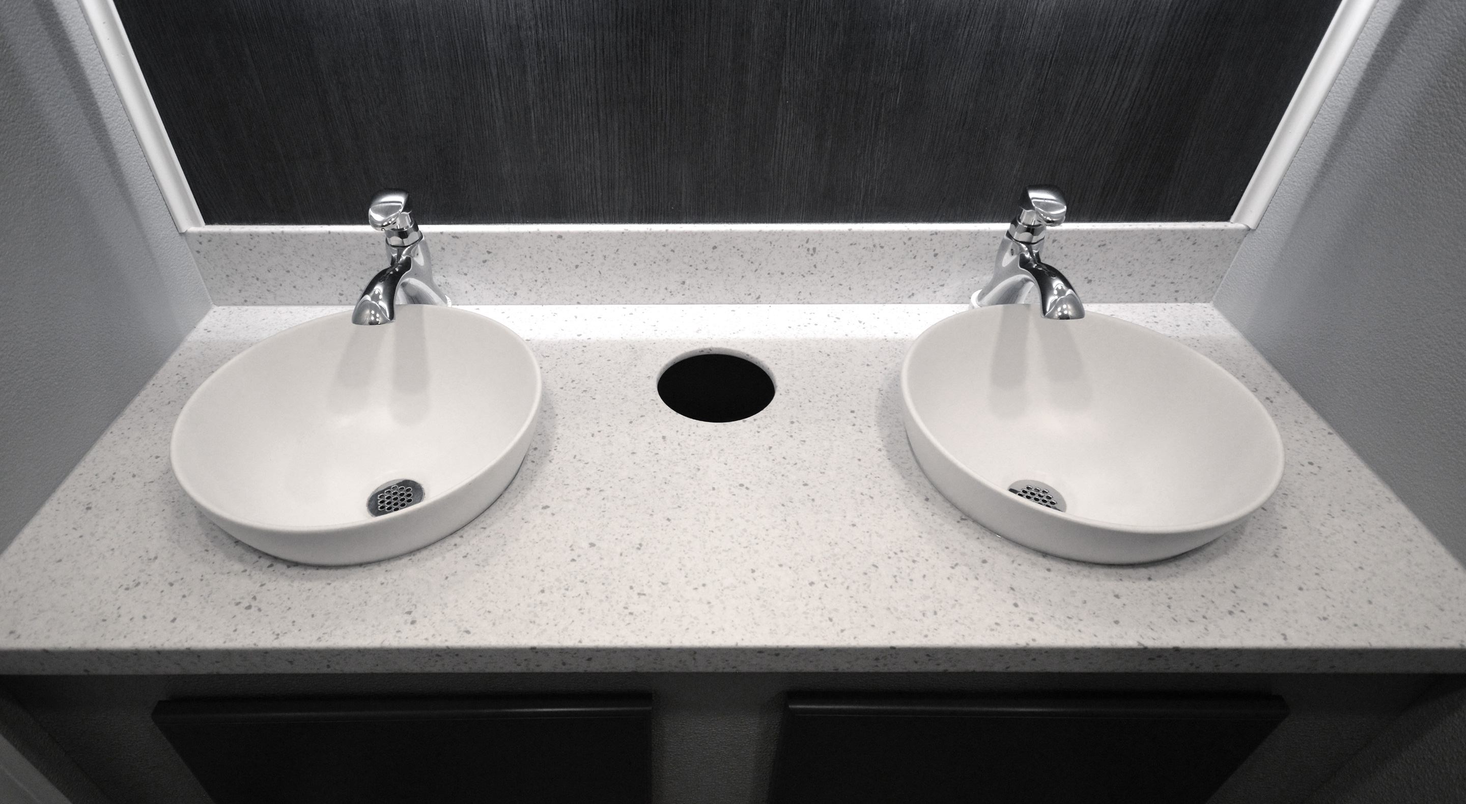 Double white oval sinks with chrome faucets on a speckled white countertop and dark backsplash.