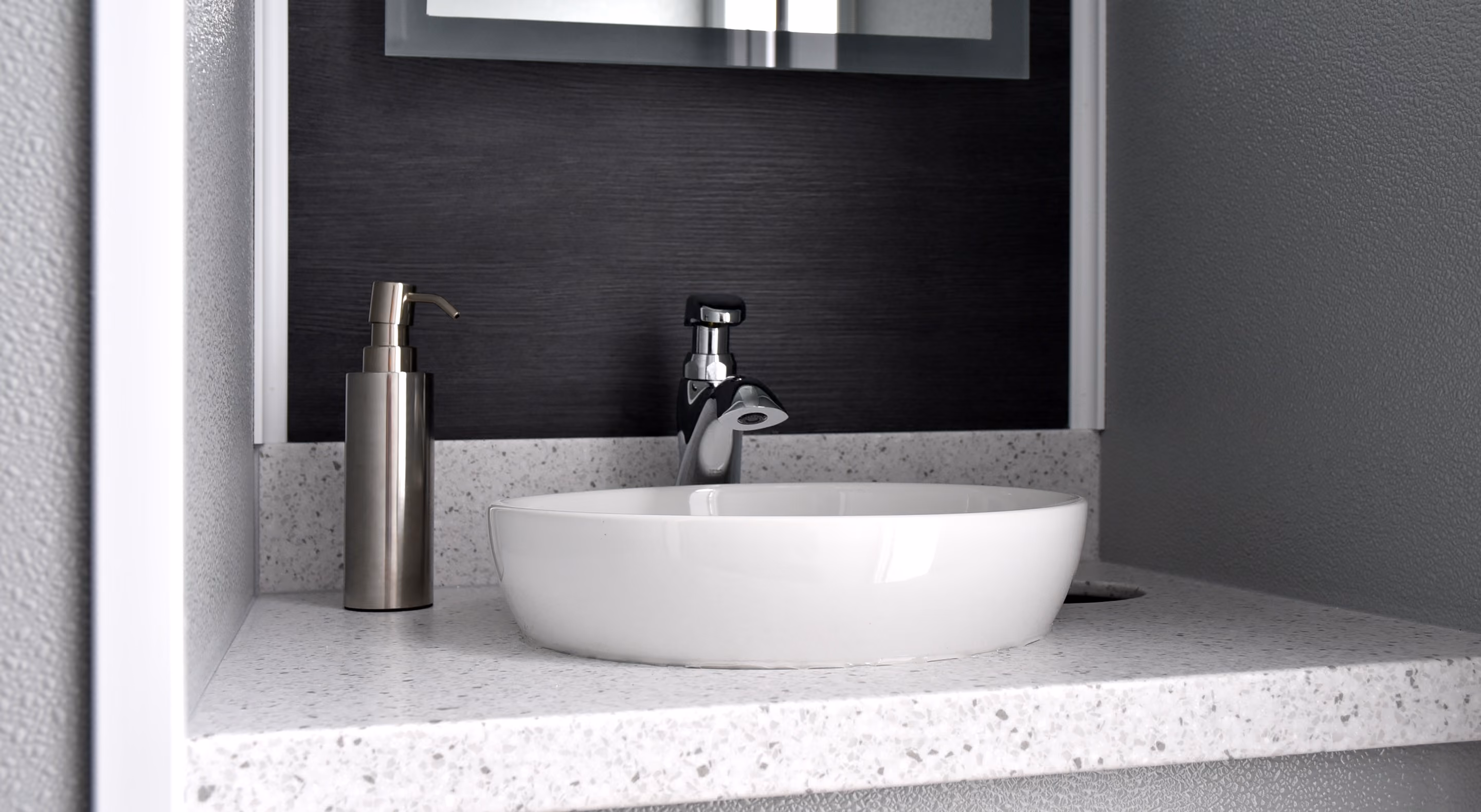Modern bathroom sink setup featuring a round white basin, sleek faucet, and a silver soap dispenser.