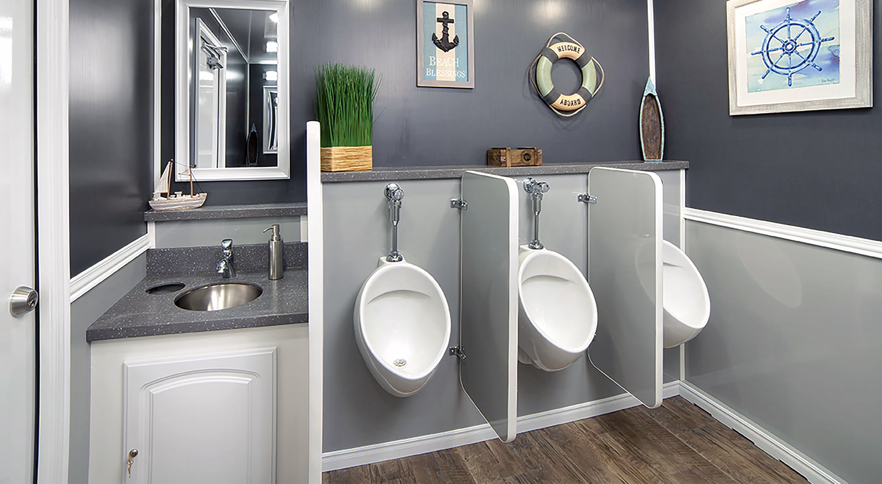 Modern male restroom with three urinals separated by gray partitions and a sink with a mirror and decor.