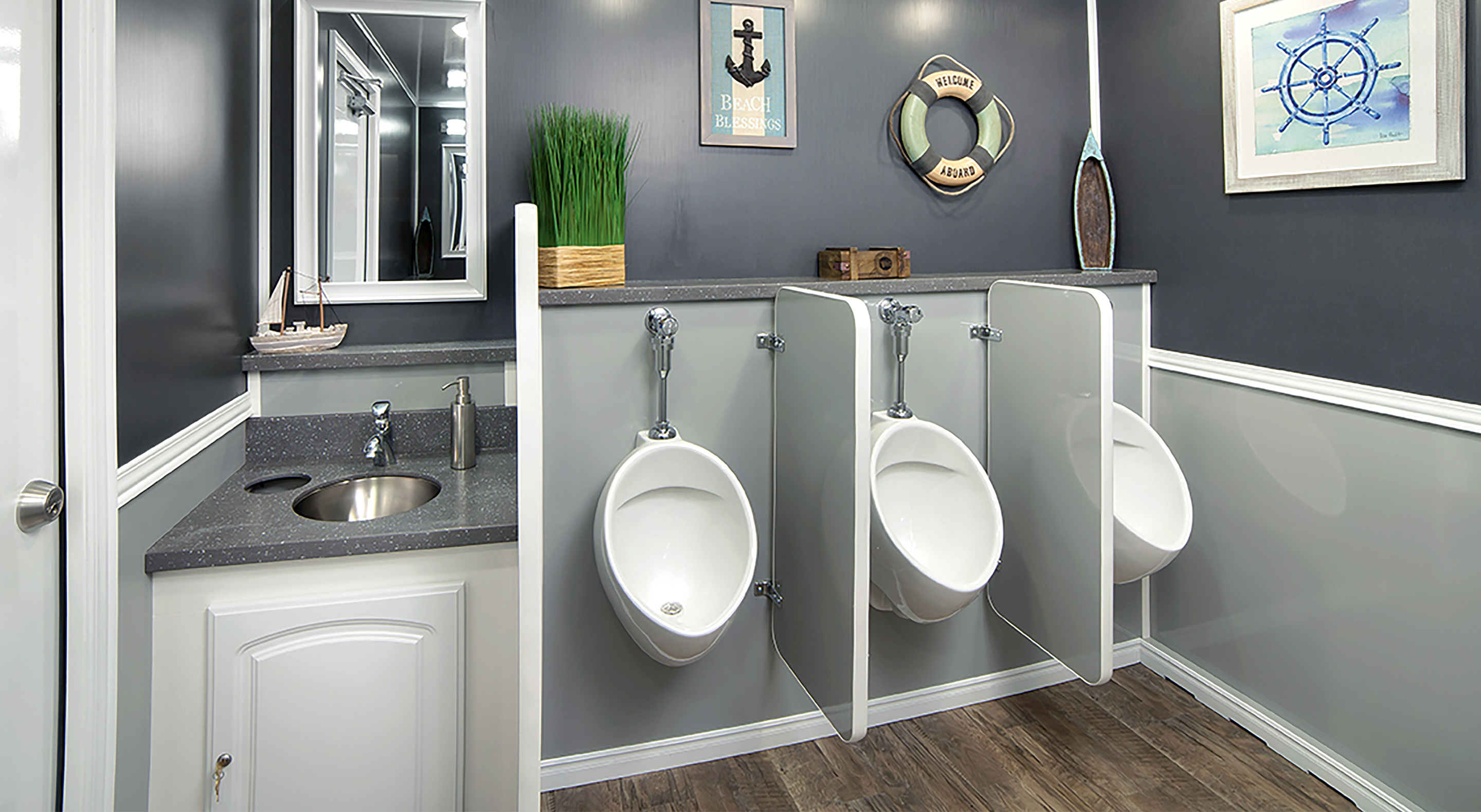 Modern male restroom with three urinals separated by gray partitions and a sink with a mirror and decor.