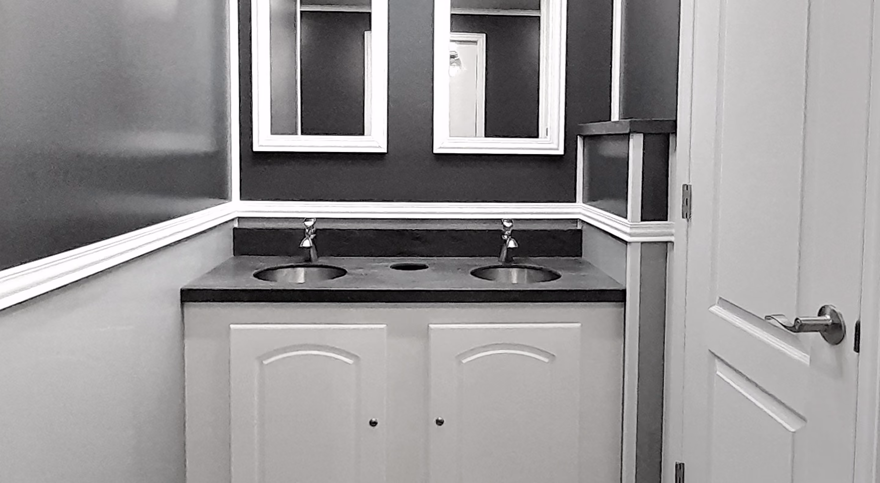 Bathroom vanity with double sinks, two mirrors above, and a partially open door on the right.