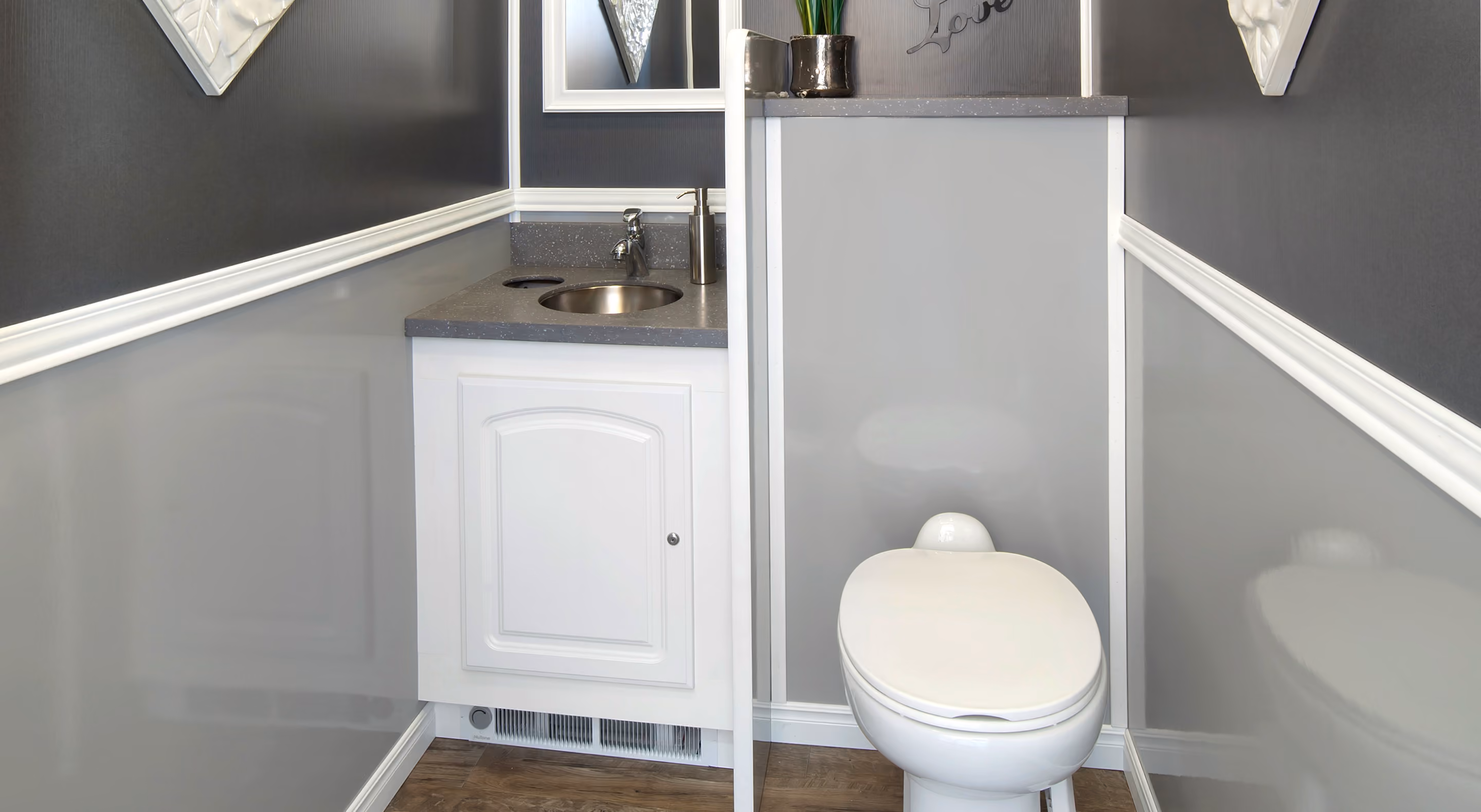 Small modern bathroom with white toilet, gray walls, a sink with gray countertop, and wooden floor.