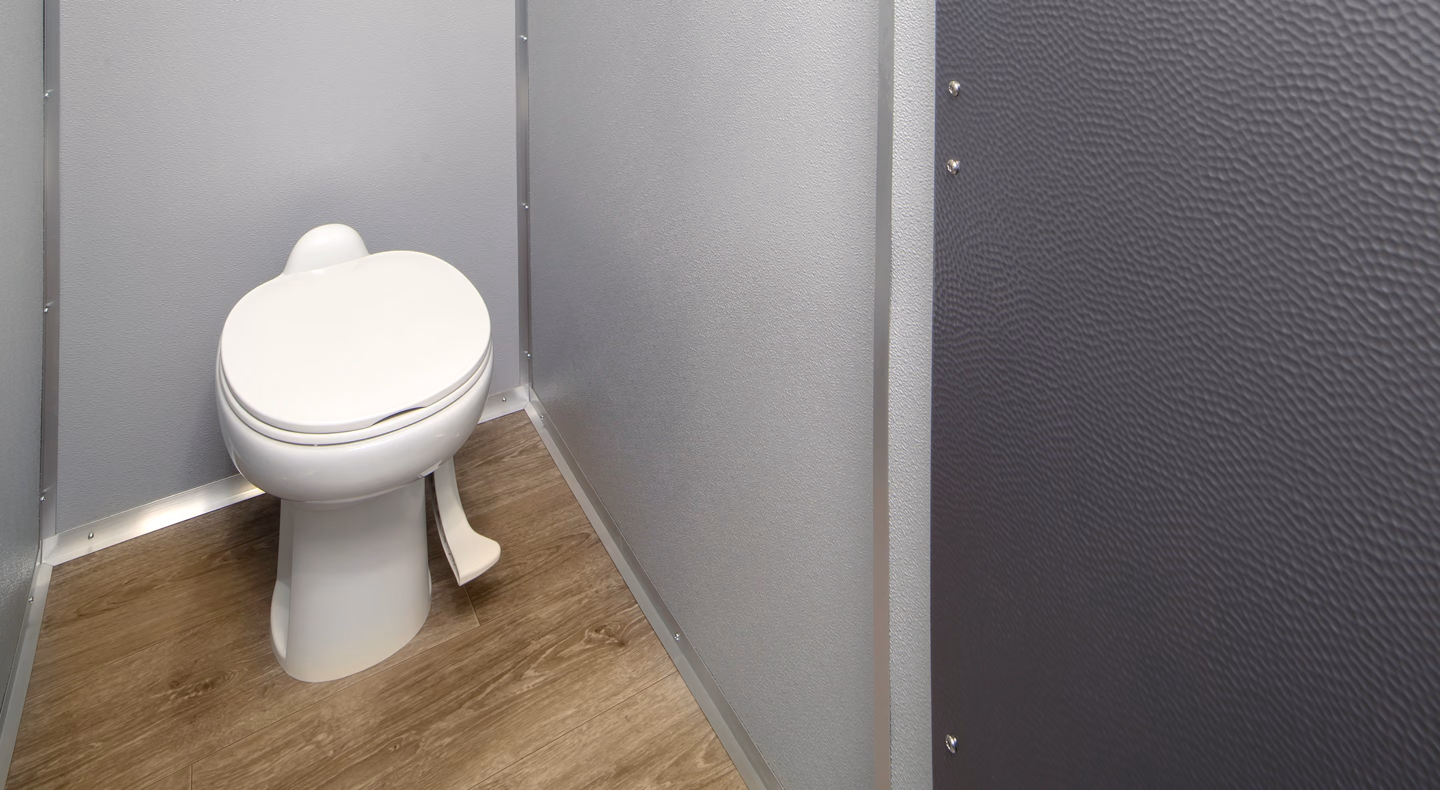 White toilet in a gray privacy stall with textured walls and wooden floor.