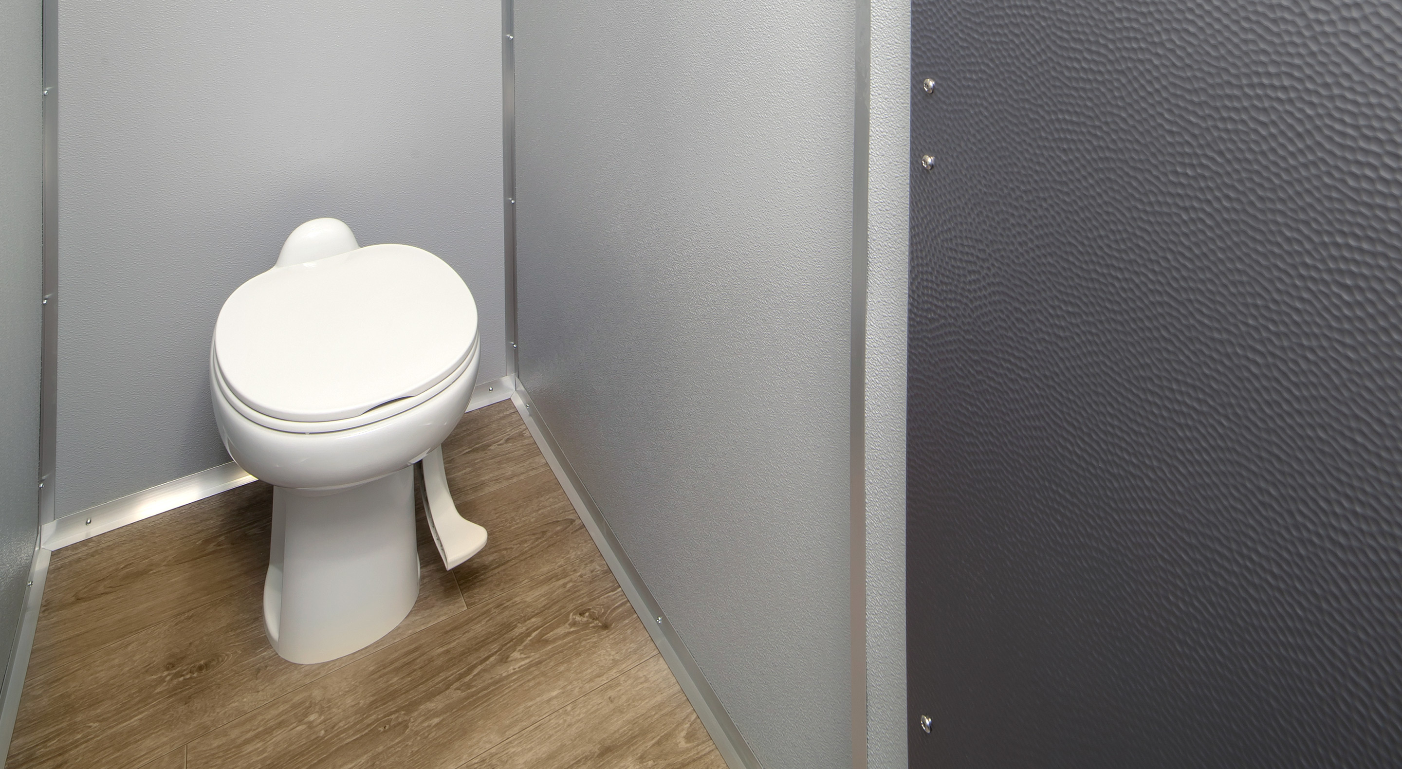 White toilet in a gray privacy stall with textured walls and wooden floor.