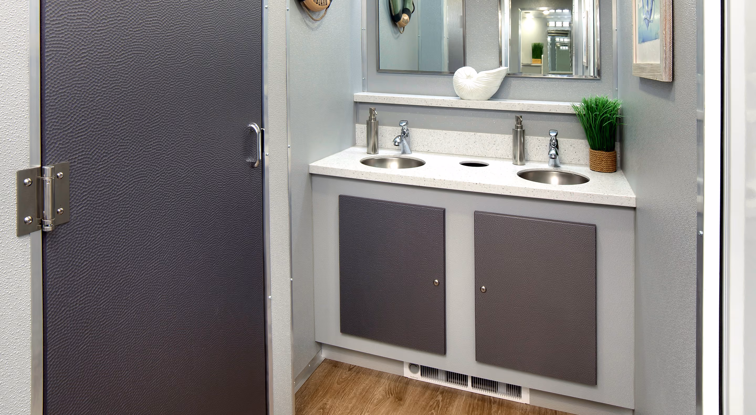 Modern bathroom with two round sinks, gray cabinets, a large mirror, and decorative plants on countertop.