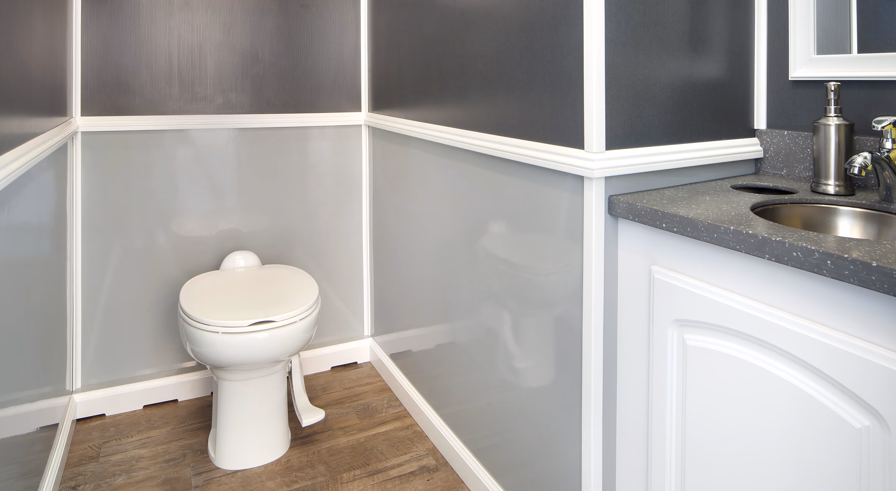 Small bathroom corner with a white toilet, gray paneled walls, wood floor, and a sink countertop.