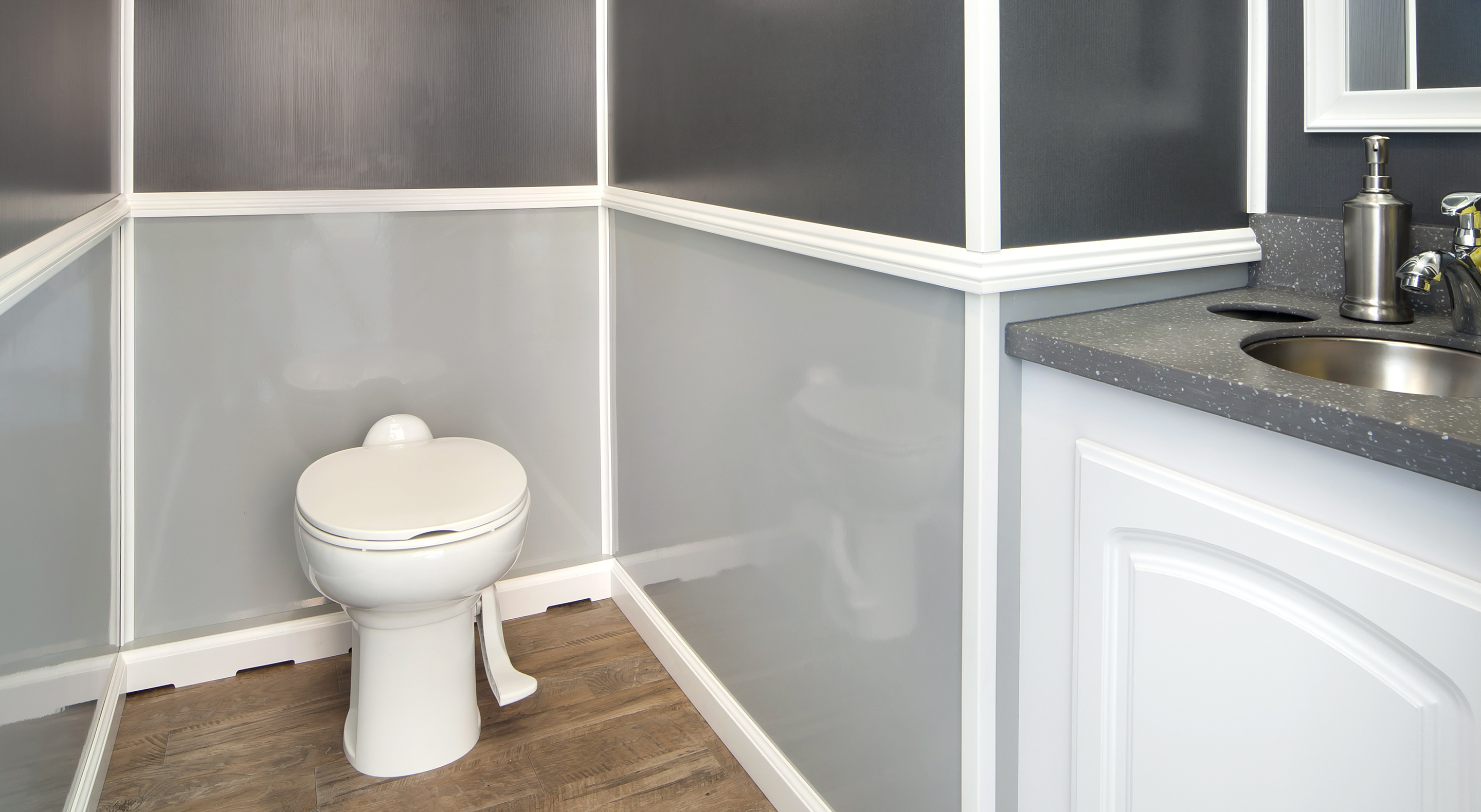 Small bathroom corner with a white toilet, gray paneled walls, wood floor, and a sink countertop.