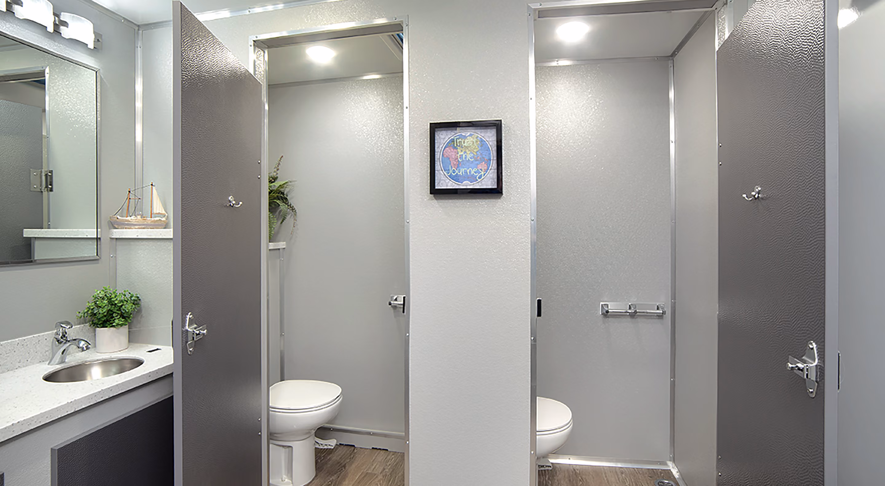 Two individual restroom stalls with gray doors, a sink, and framed artwork on the wall.