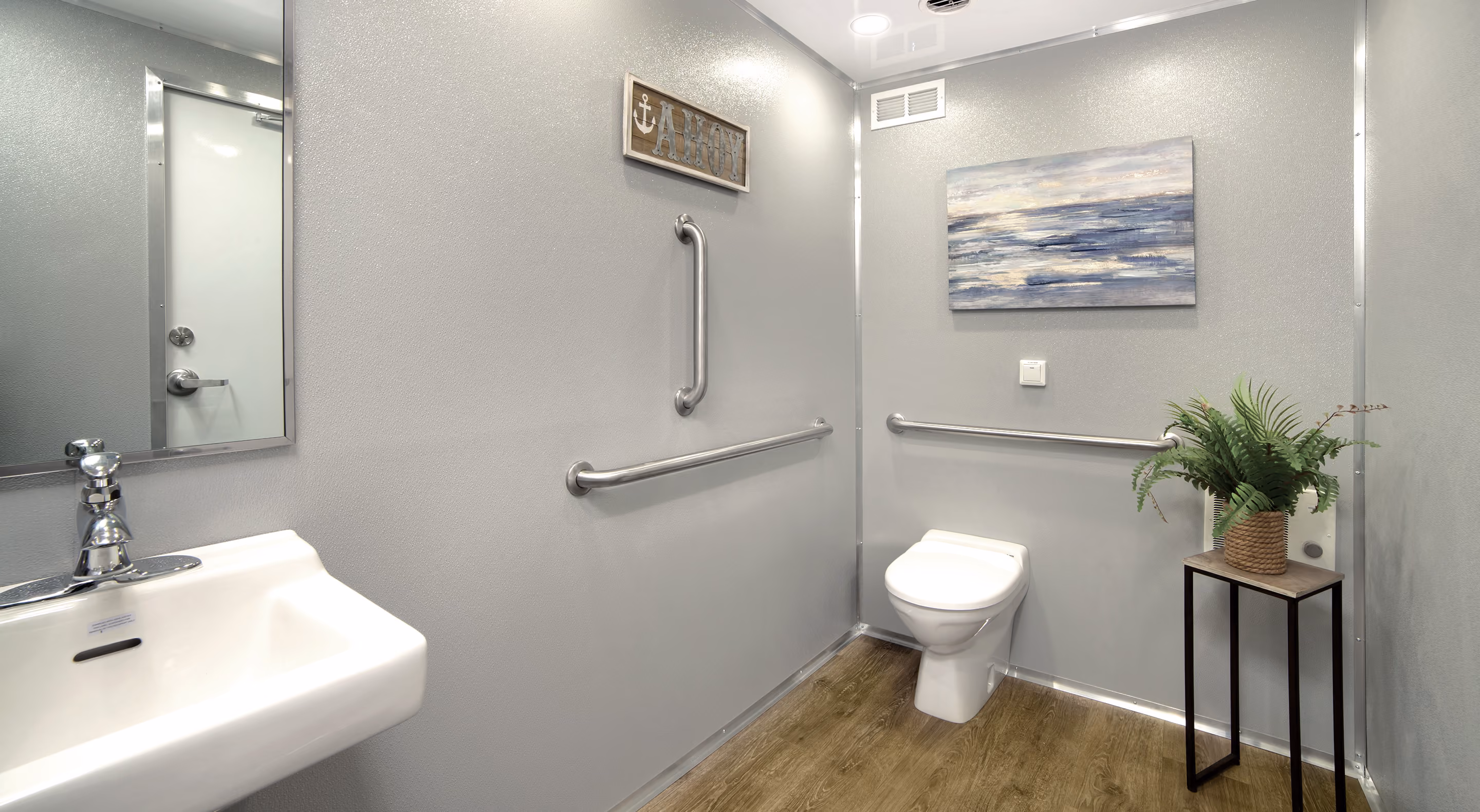 Accessible restroom featuring a sink, grab bars, toilet, and a plant in a modern setting.