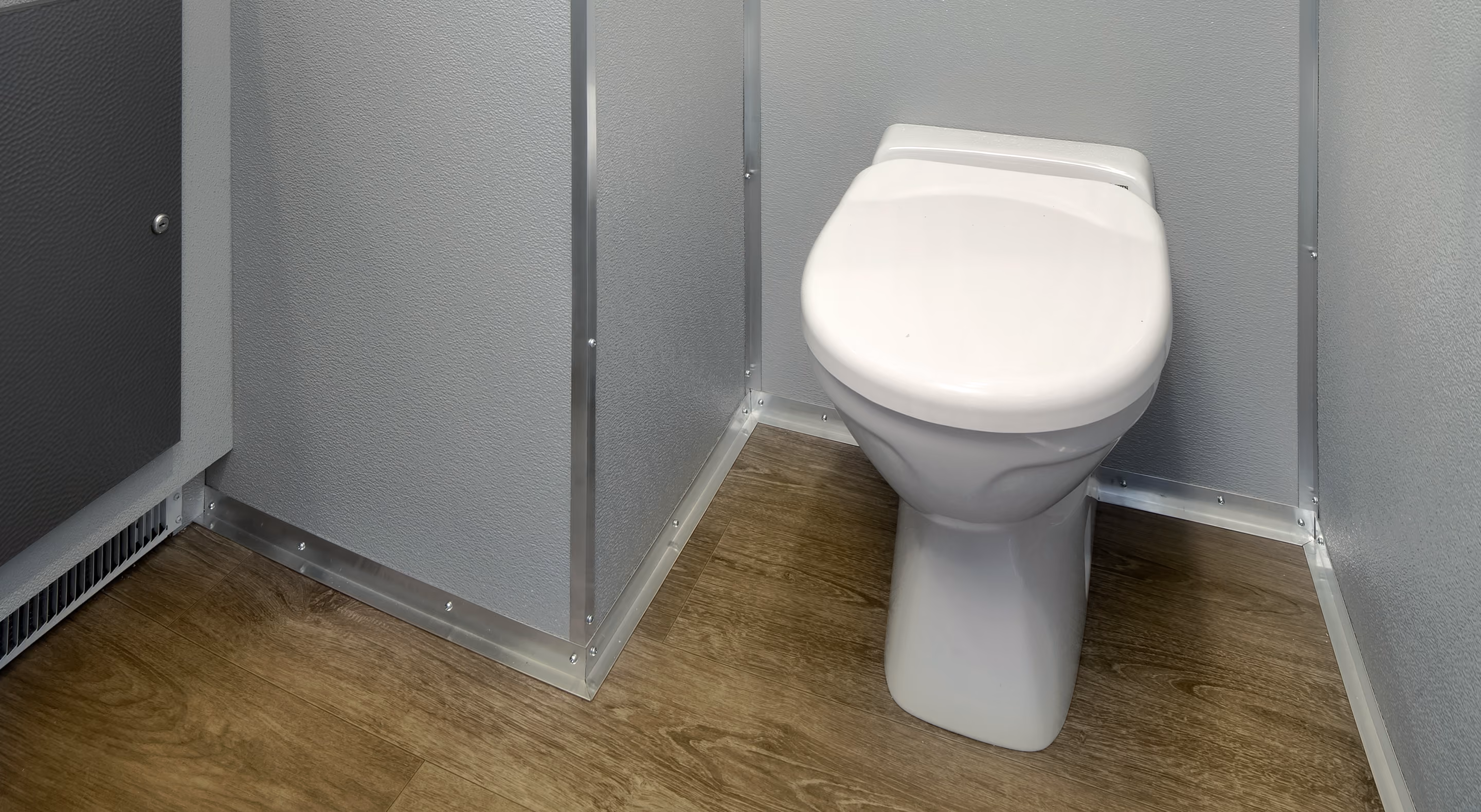 White toilet in a small room with gray walls and wood-look vinyl flooring.