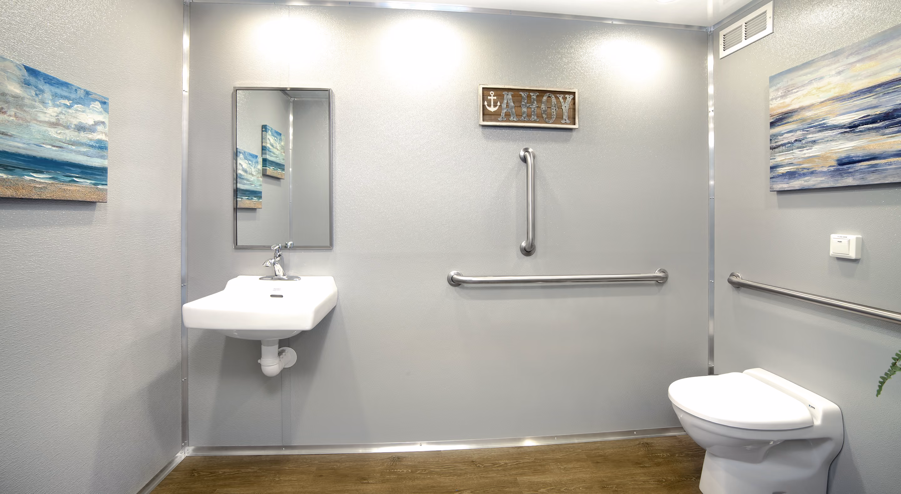 Modern restroom featuring a sink, toilet, grab bars, mirror, and nautical-themed artwork.