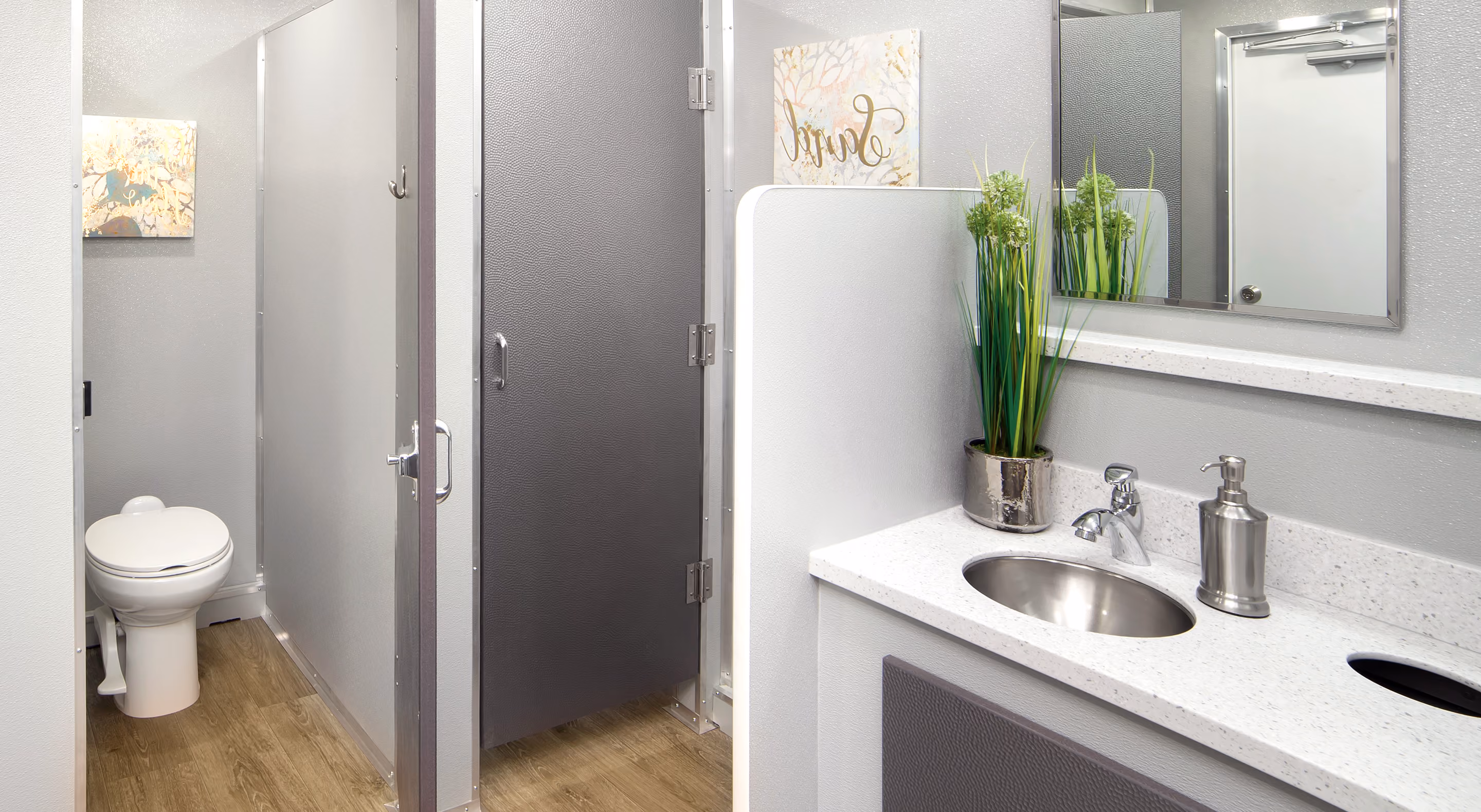 Modern restroom interior featuring a toilet, sink, and greenery; walls in gray tones.