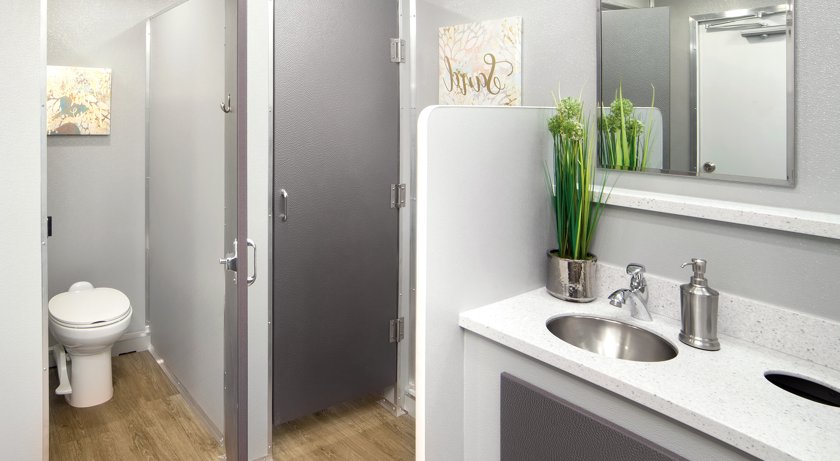 Modern restroom interior featuring a toilet, sink, and greenery; walls in gray tones.