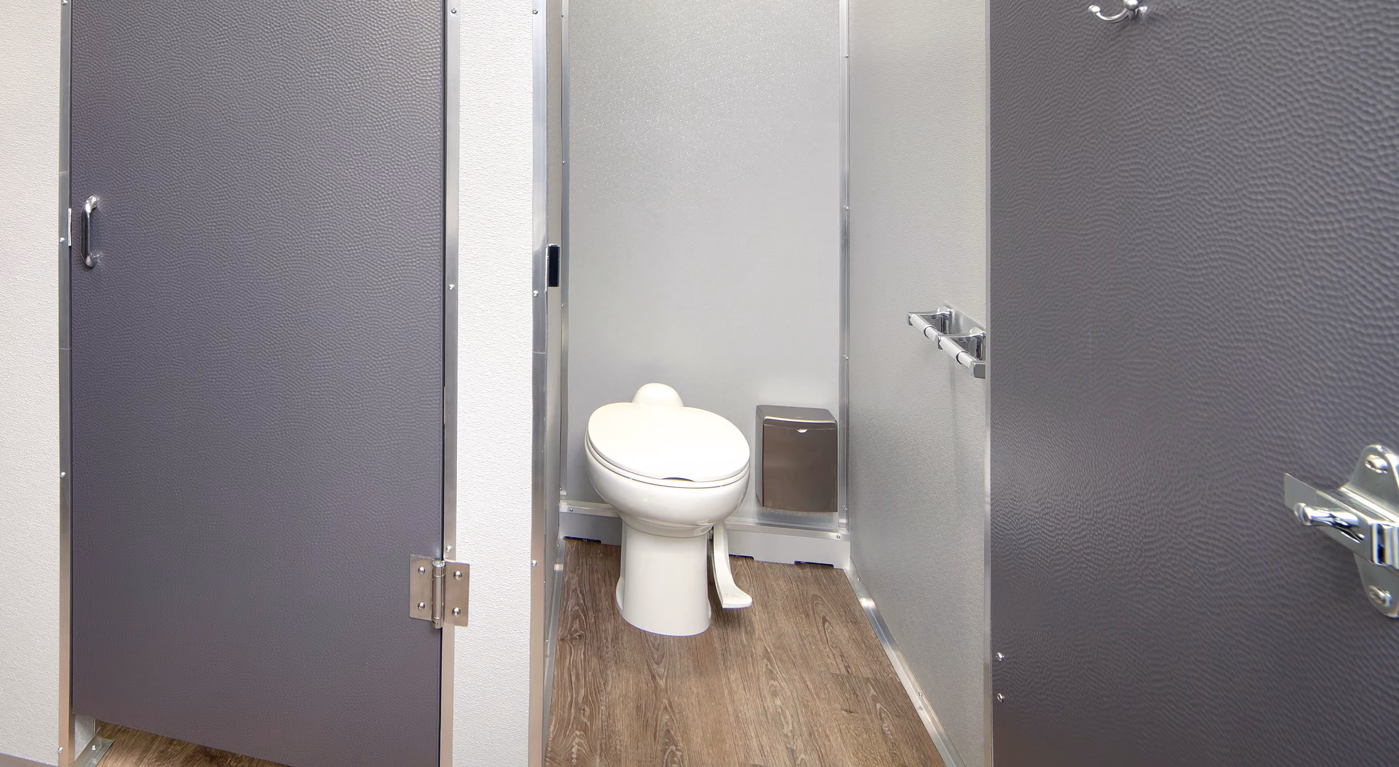 Interior of a commercial bathroom stall with a closed-lid toilet and wood-look flooring.