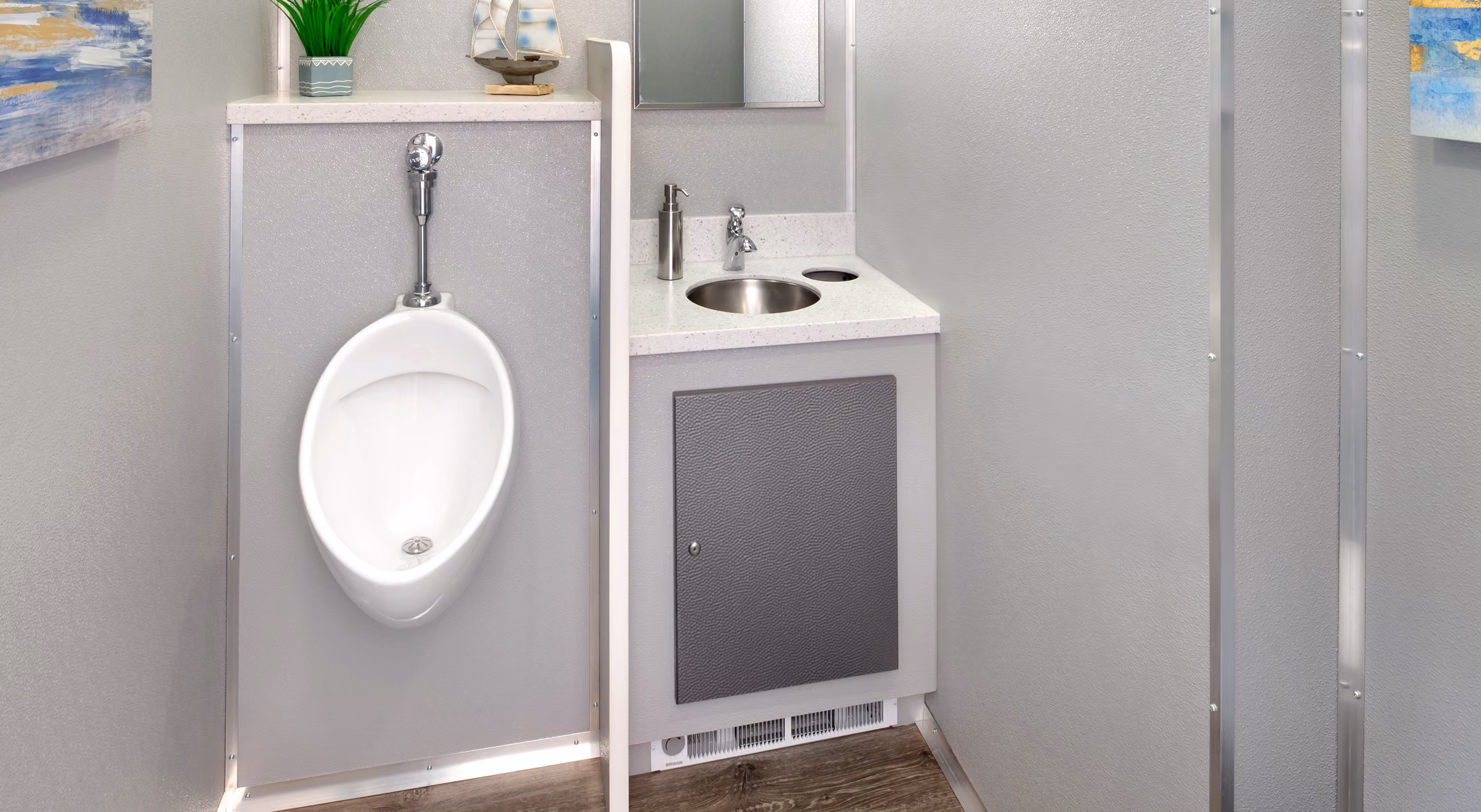 Men's restroom with a white urinal, sink, and mirror against a gray wall.