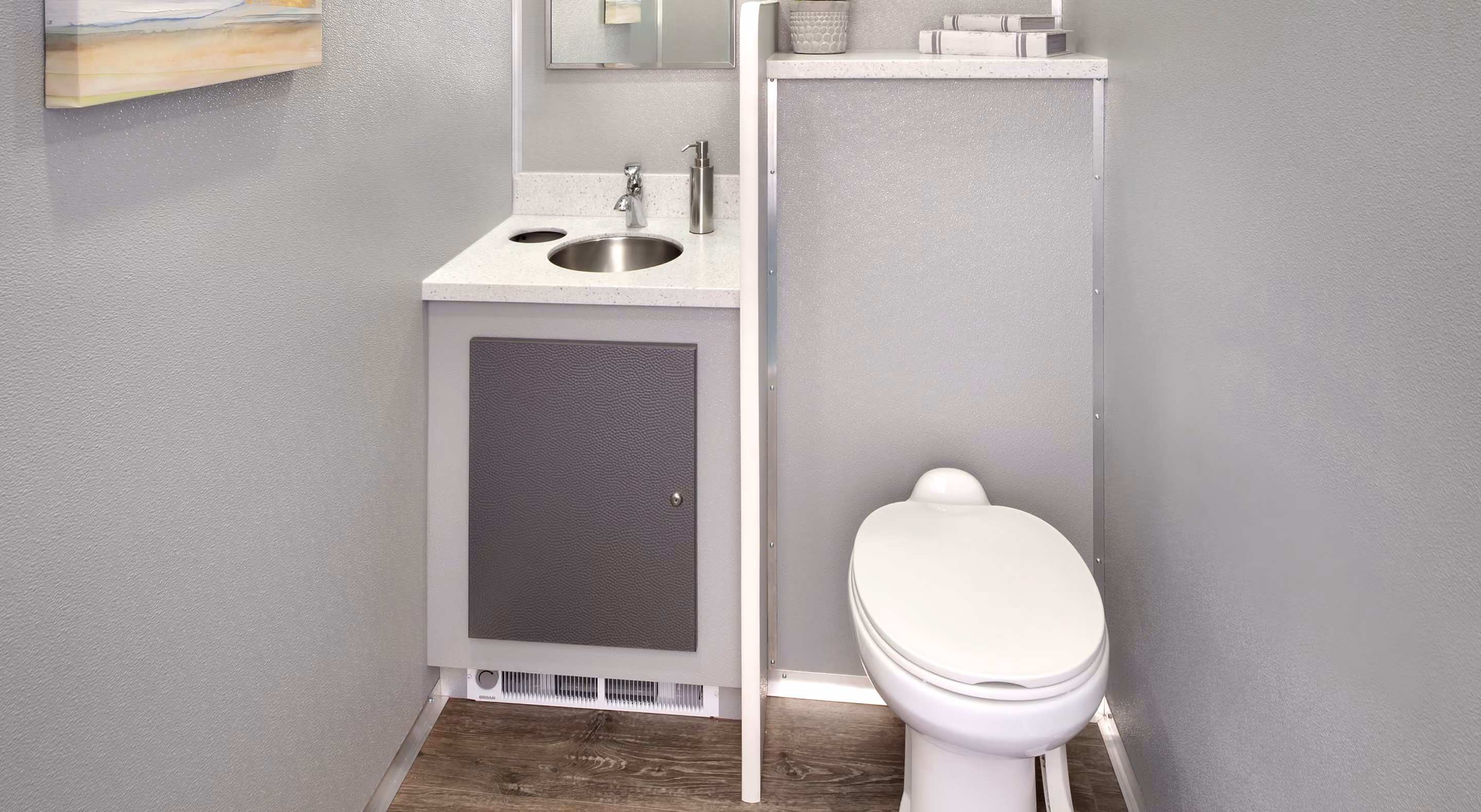 Compact restroom with a white toilet, vanity sink, and light gray walls with wood flooring.