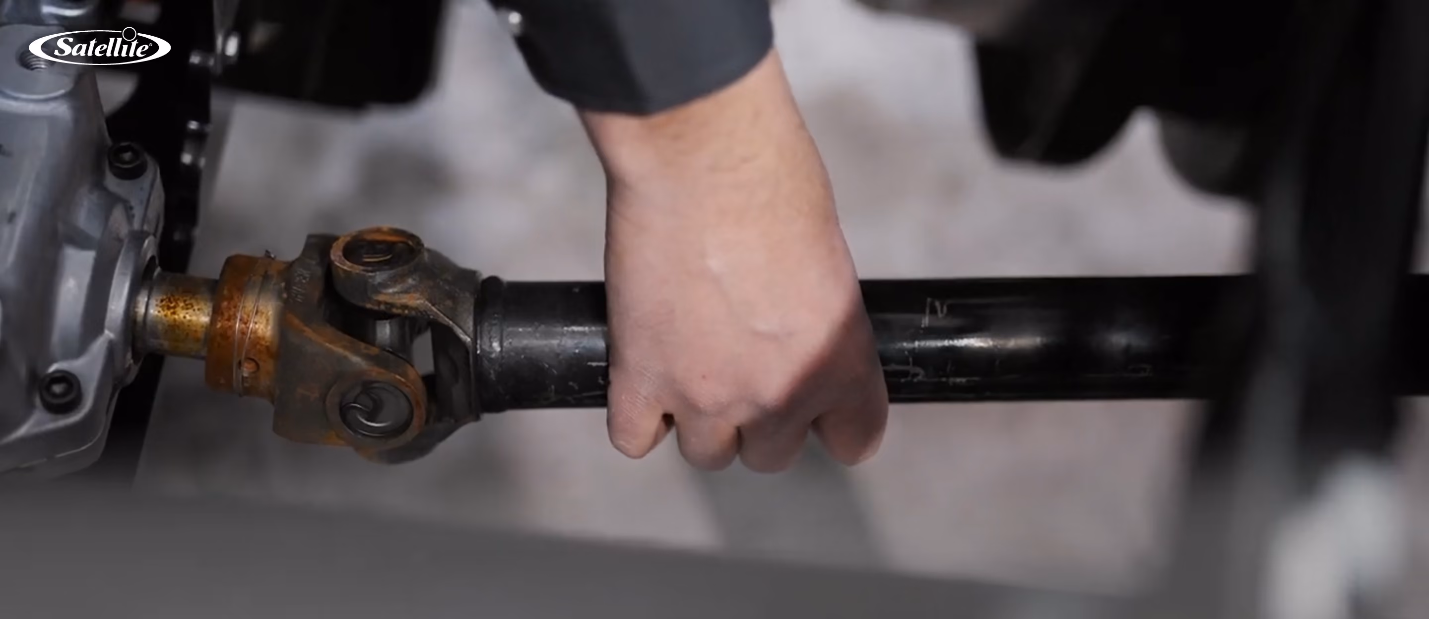 Close-up of a technician inspecting and servicing a driveshaft on a portable sanitation service truck. The image represents preventative maintenance for portable restroom service vehicles, restroom trailers, handwash stations, and portable sanitation equipment to improve reliability, extend equipment life, and reduce downtime.