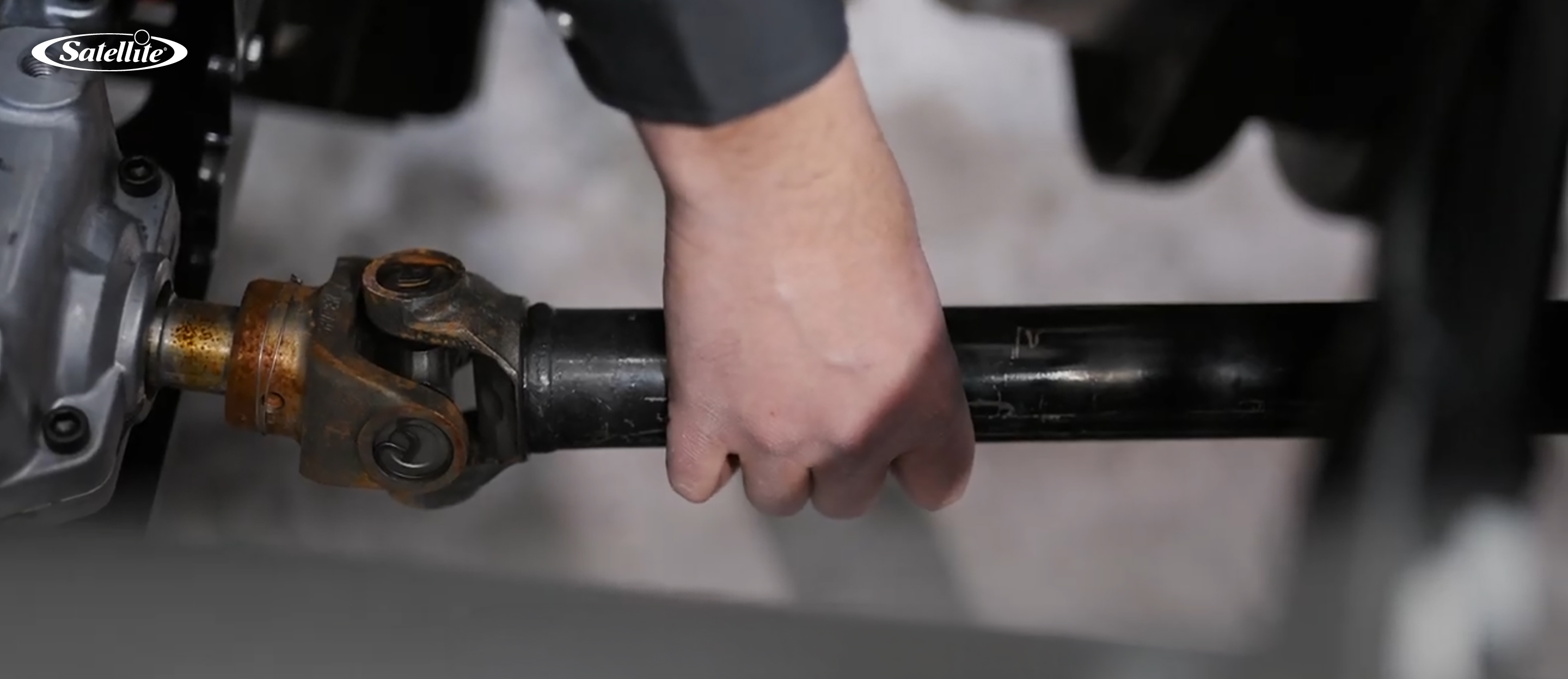 Close-up of a technician inspecting and servicing a driveshaft on a portable sanitation service truck. The image represents preventative maintenance for portable restroom service vehicles, restroom trailers, handwash stations, and portable sanitation equipment to improve reliability, extend equipment life, and reduce downtime.
