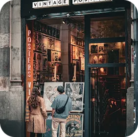 Two people looking at vintage posters displayed outside an art shop.