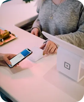 Person using a smartphone to make a contactless payment at a store checkout with a white payment terminal.