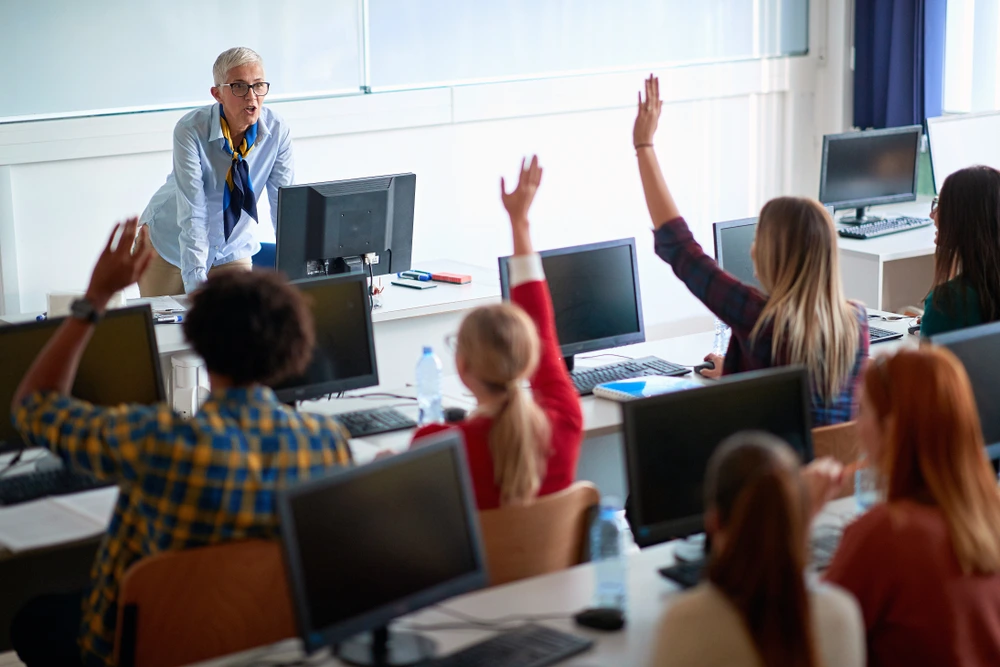 Students raising hand at the front of the classroom