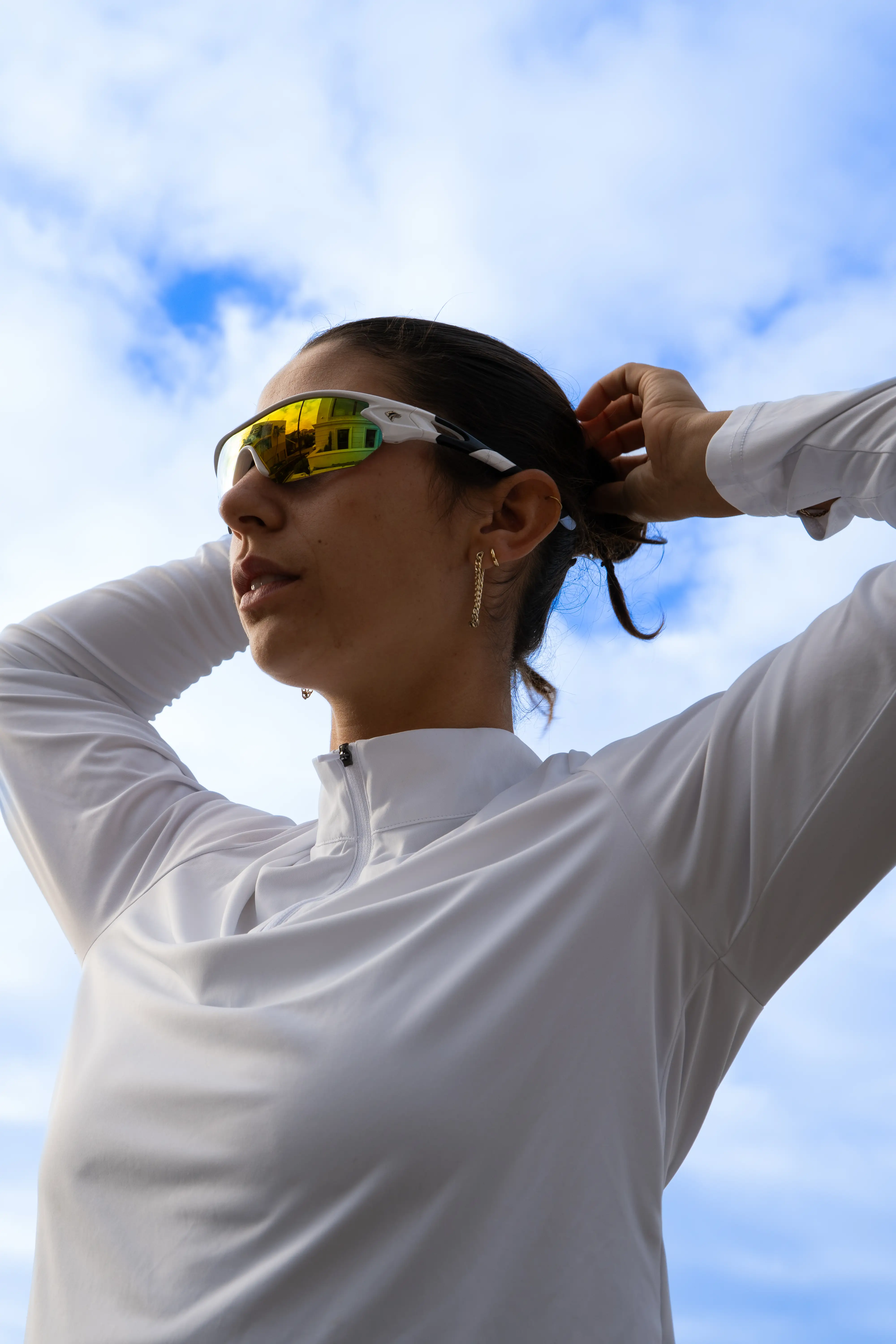 A girl fixing her hair wearing large athletic sunglasses.