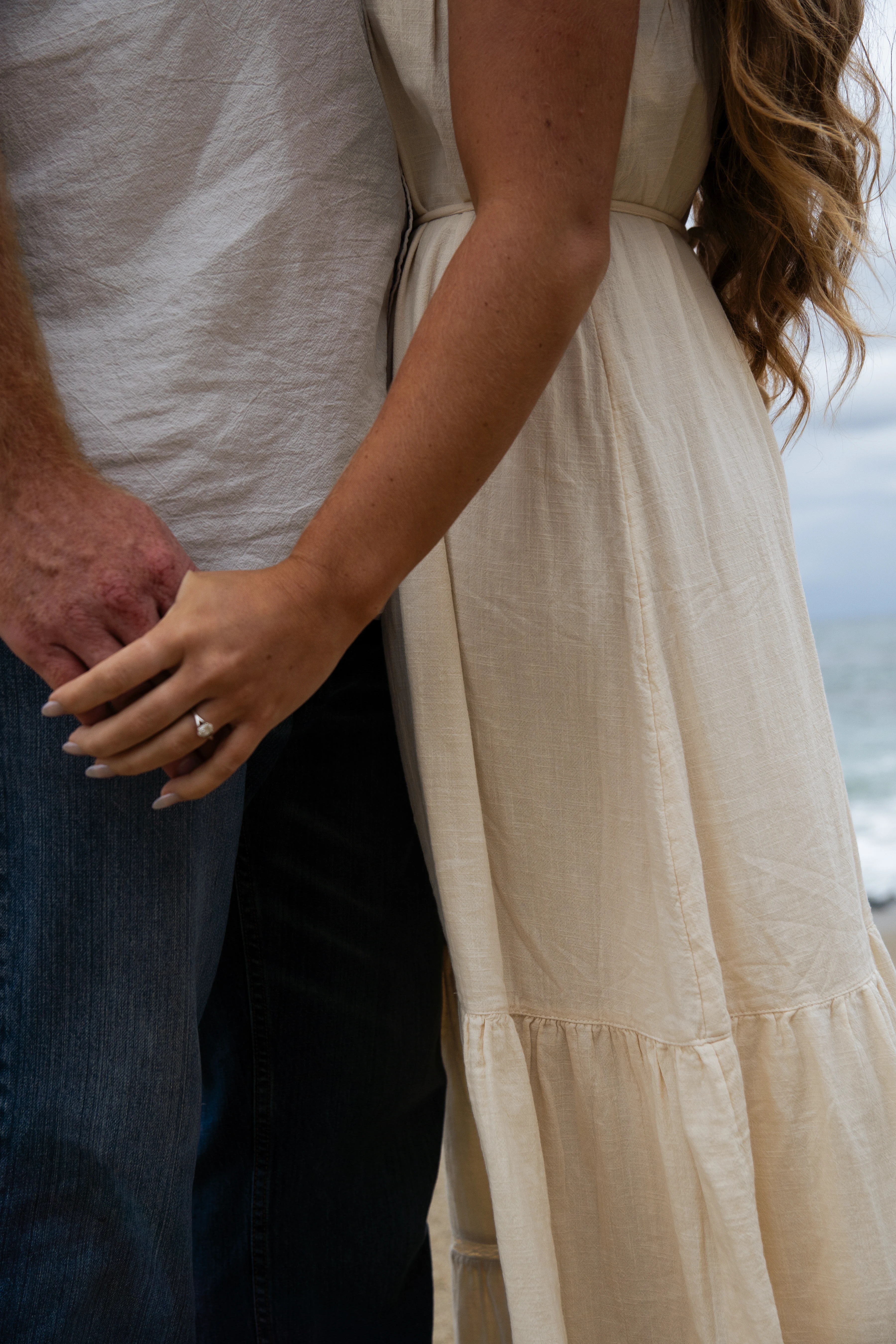A newly engaged couple holding hands, facing each other.