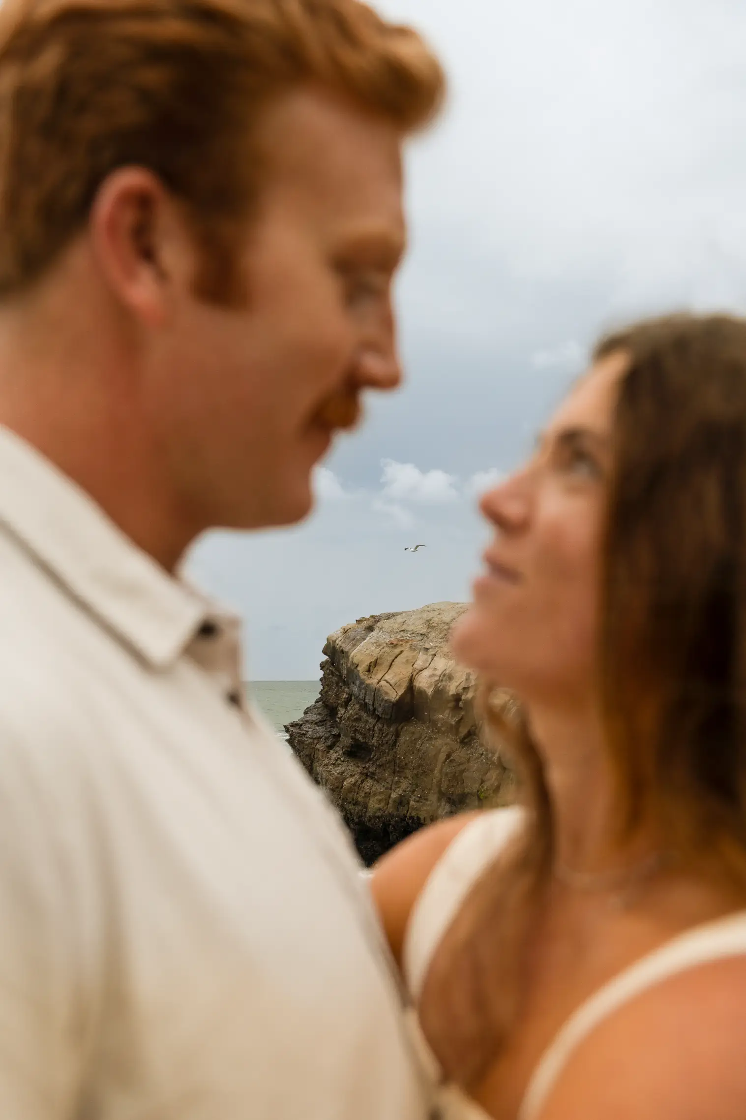 A beautiful couple looking into each other's eyes along the coast.