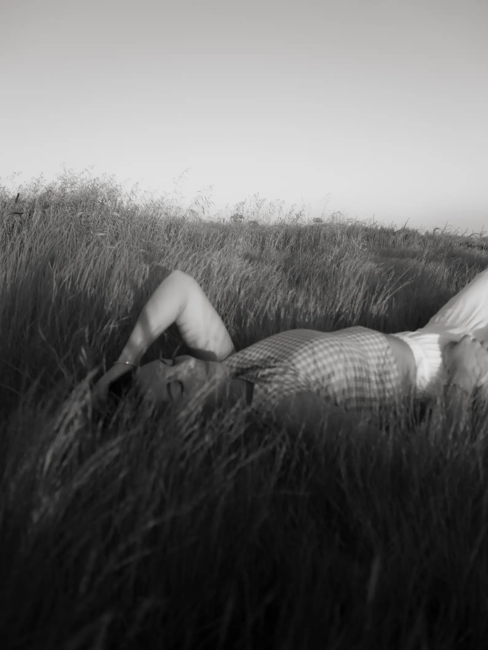 Woman lying relaxed in tall grass in a field, eyes closed, in black and white photo.