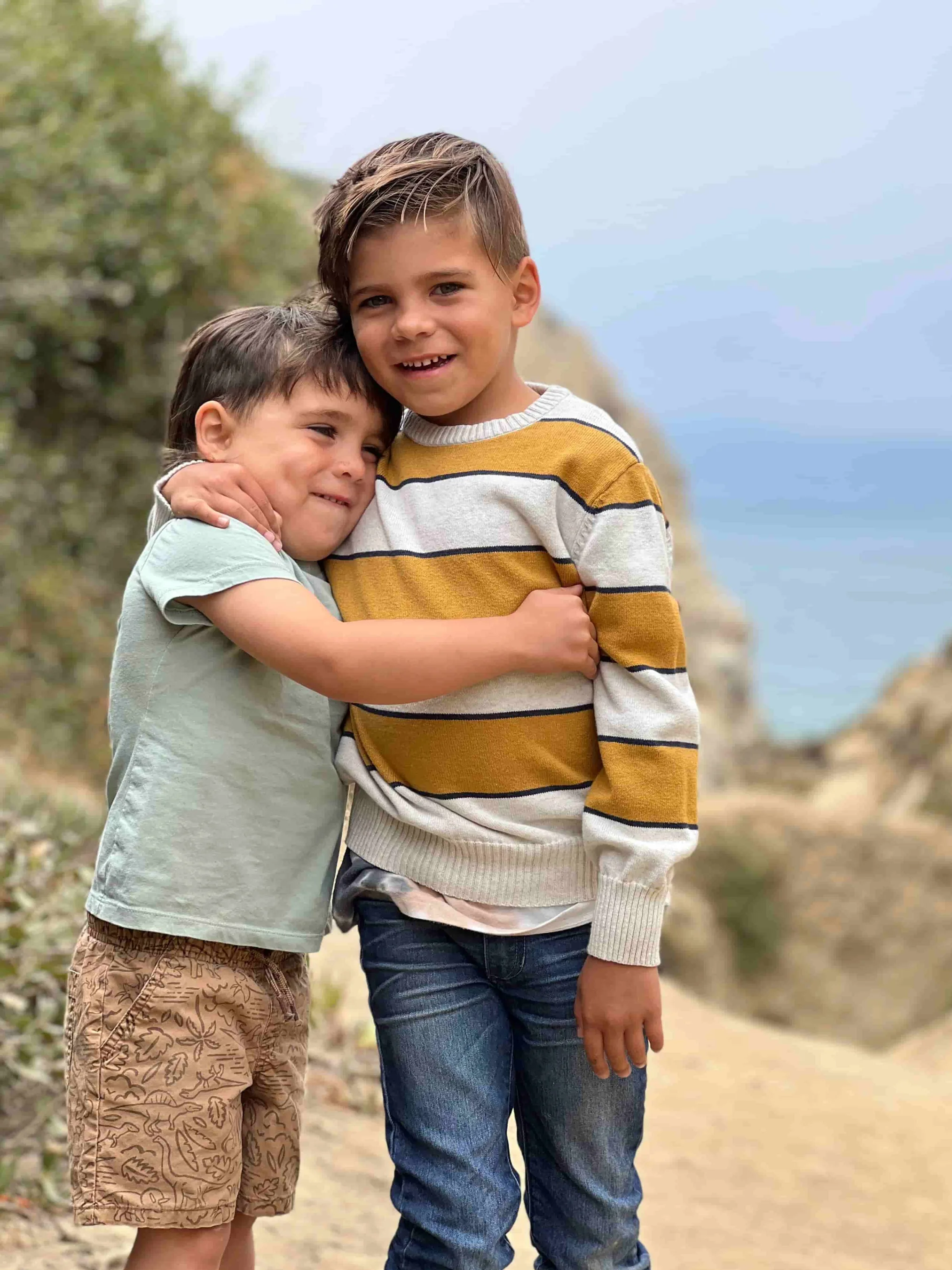 Two young brothers share a heartfelt hug along a coastal path.