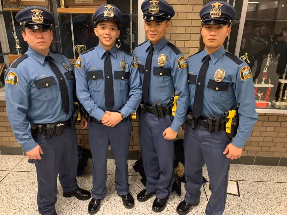 Four police officers in blue uniforms standing side by side indoors with trophies displayed behind them.