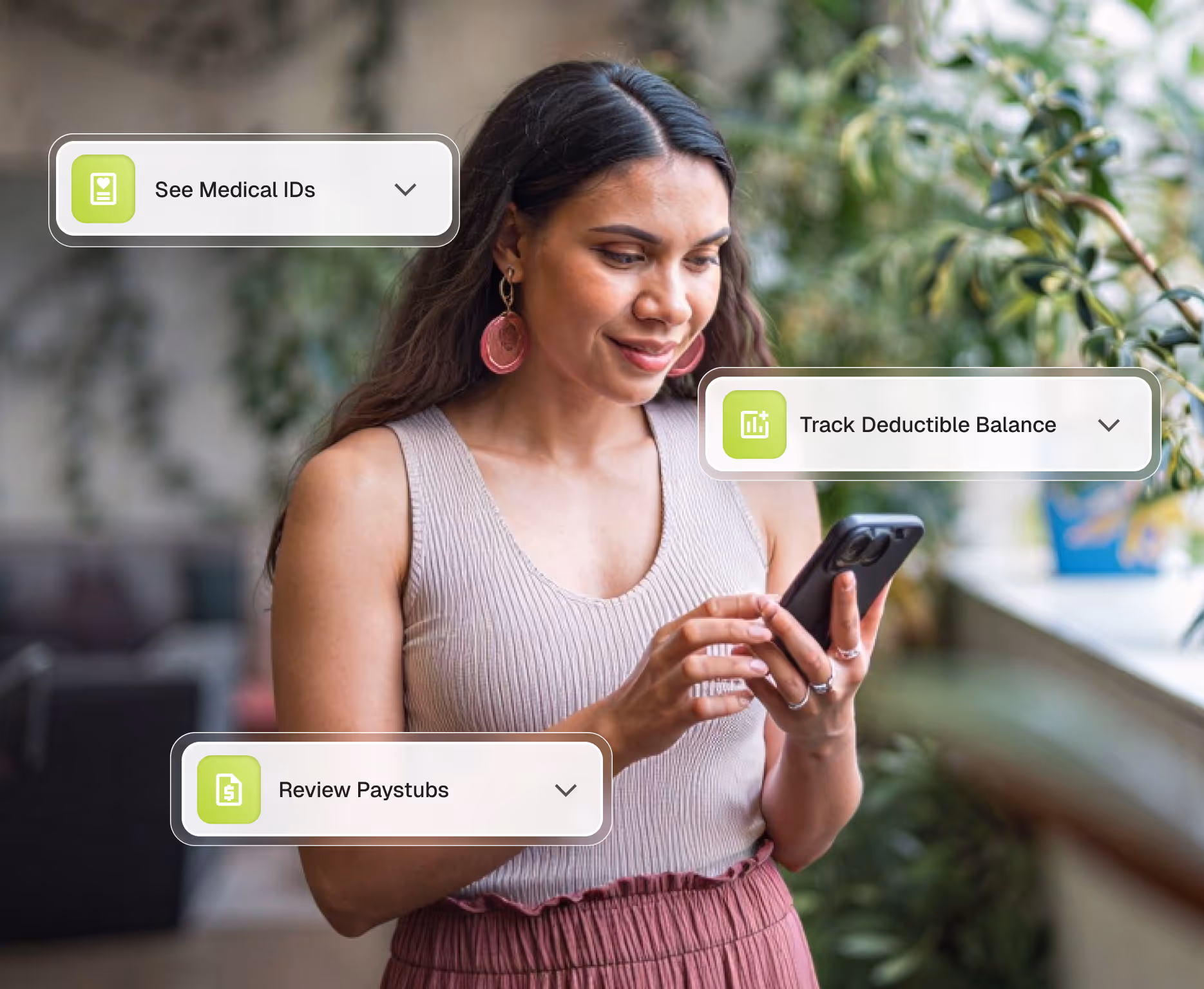 Smiling woman with long dark hair and pink earrings using a smartphone indoors with captions for medical IDs, deductible balance, and paystub review.