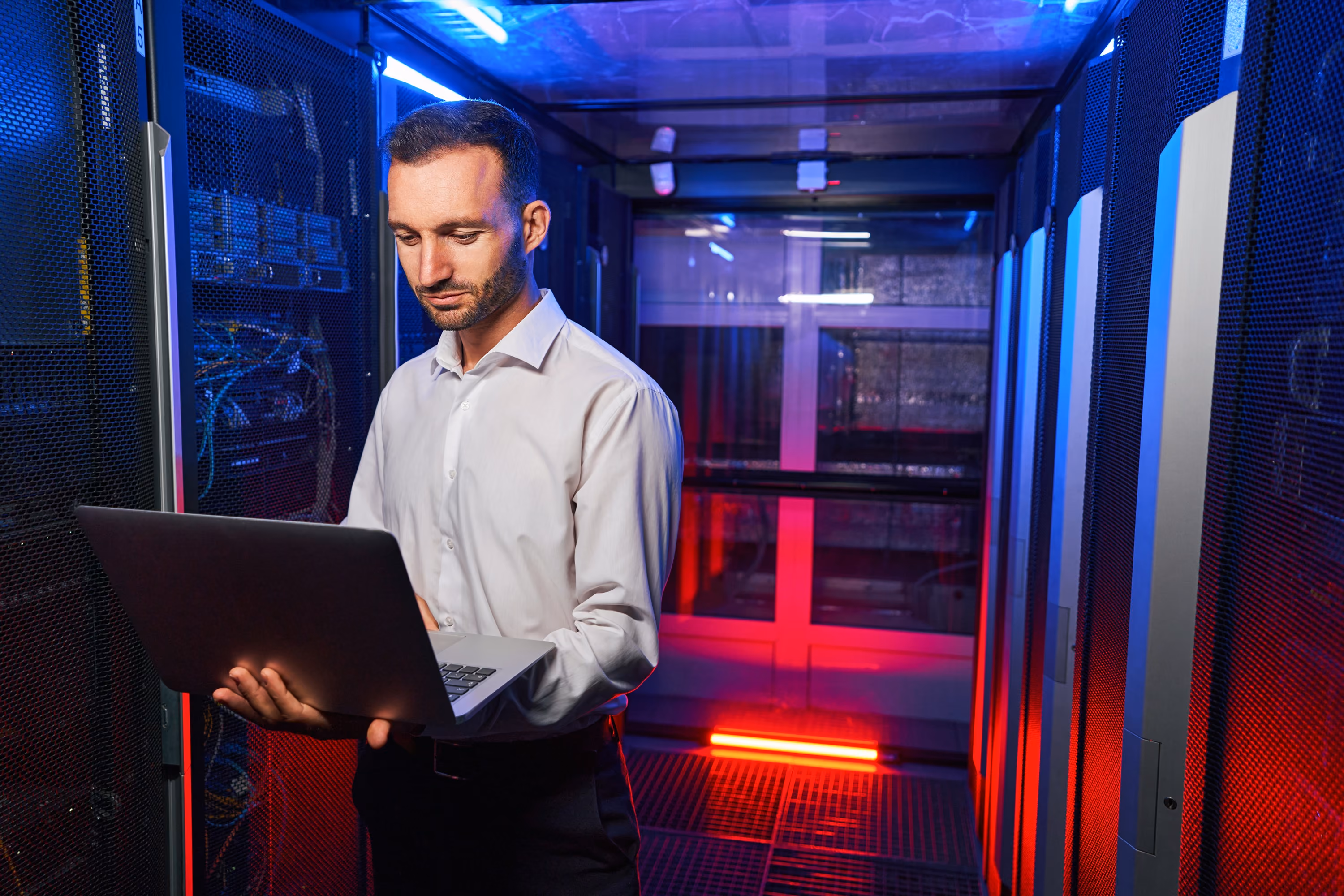 IT technician holding a laptop while checking equipment in a server room